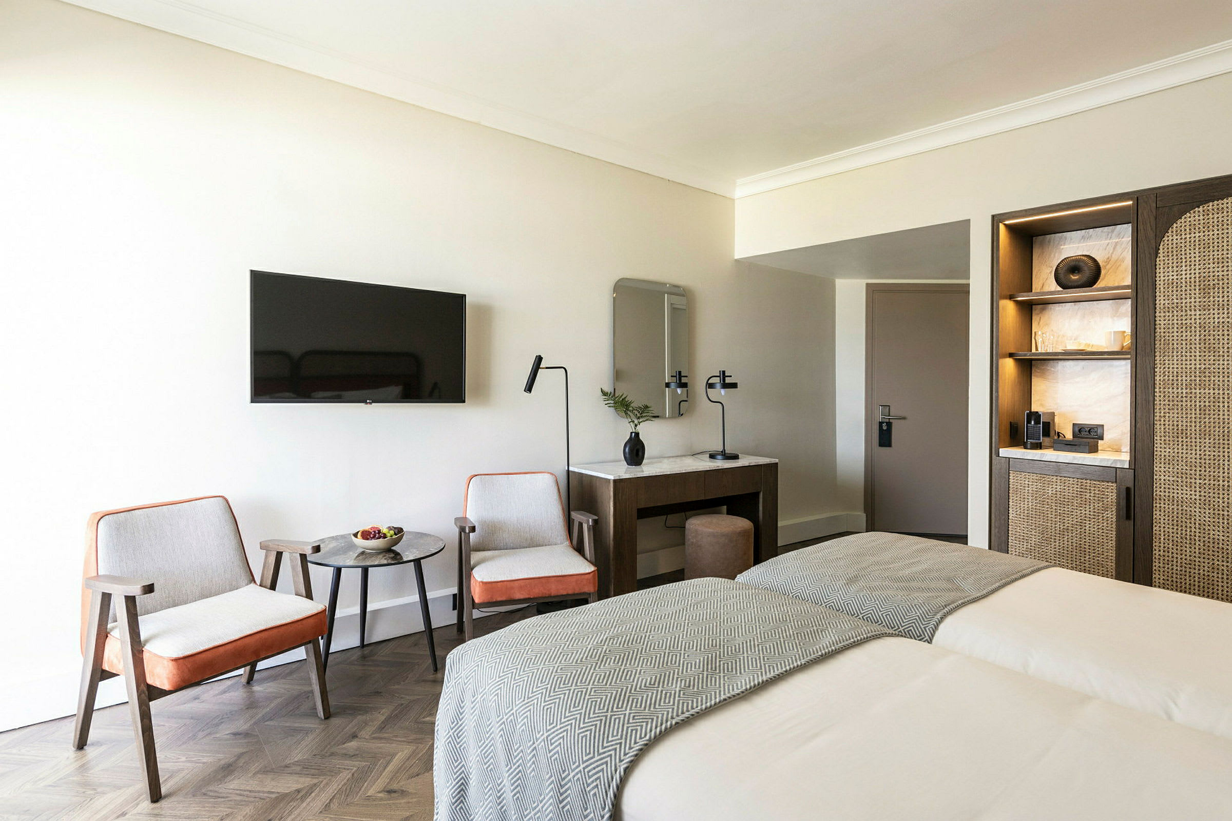 Ett hotellrum med två sängar, två stolar och ett bord framför en väggmonterad TV. (AI-genererad text)