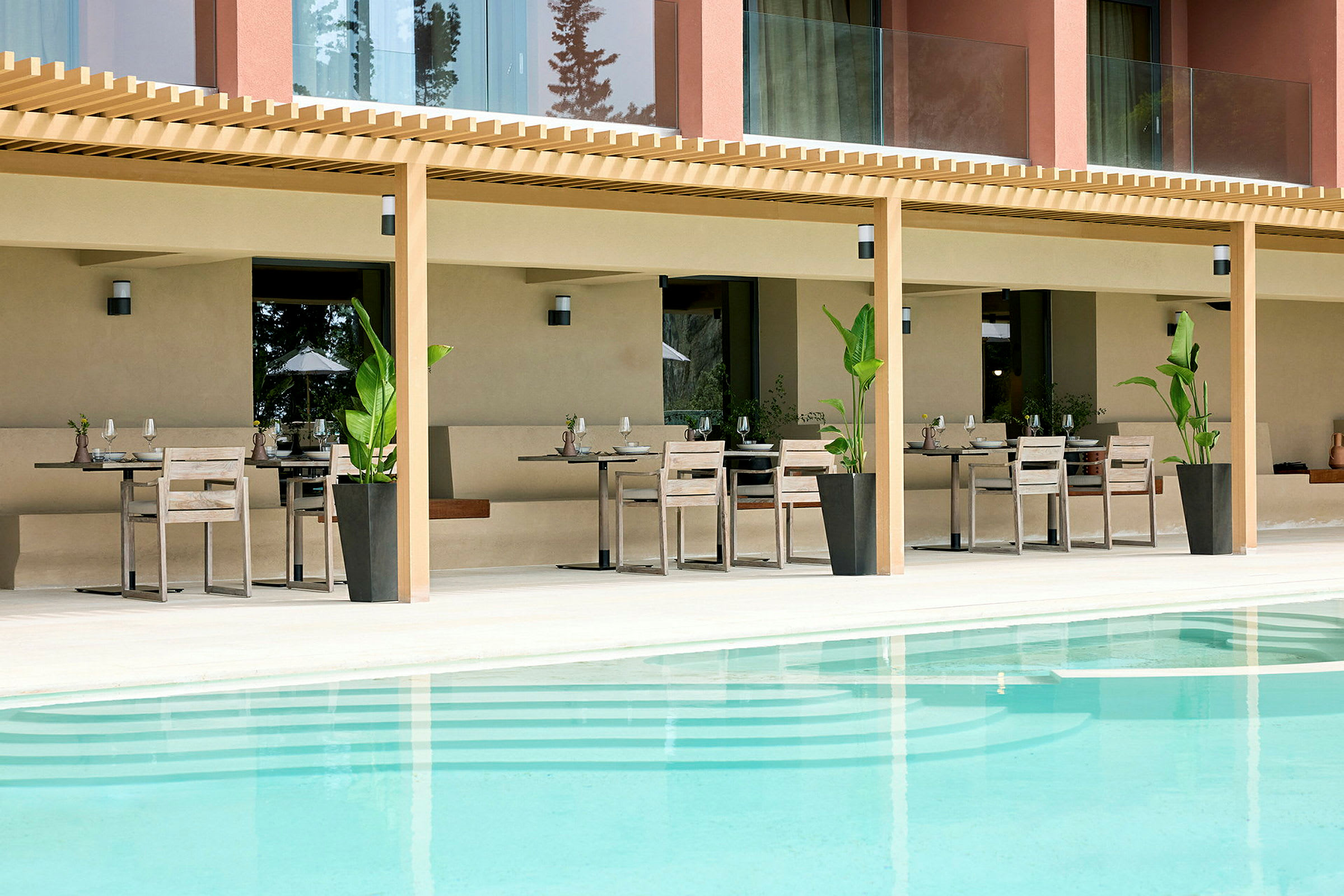 En uteservering med bord och stolar under en pergola framför en swimmingpool. (AI-genererad text)