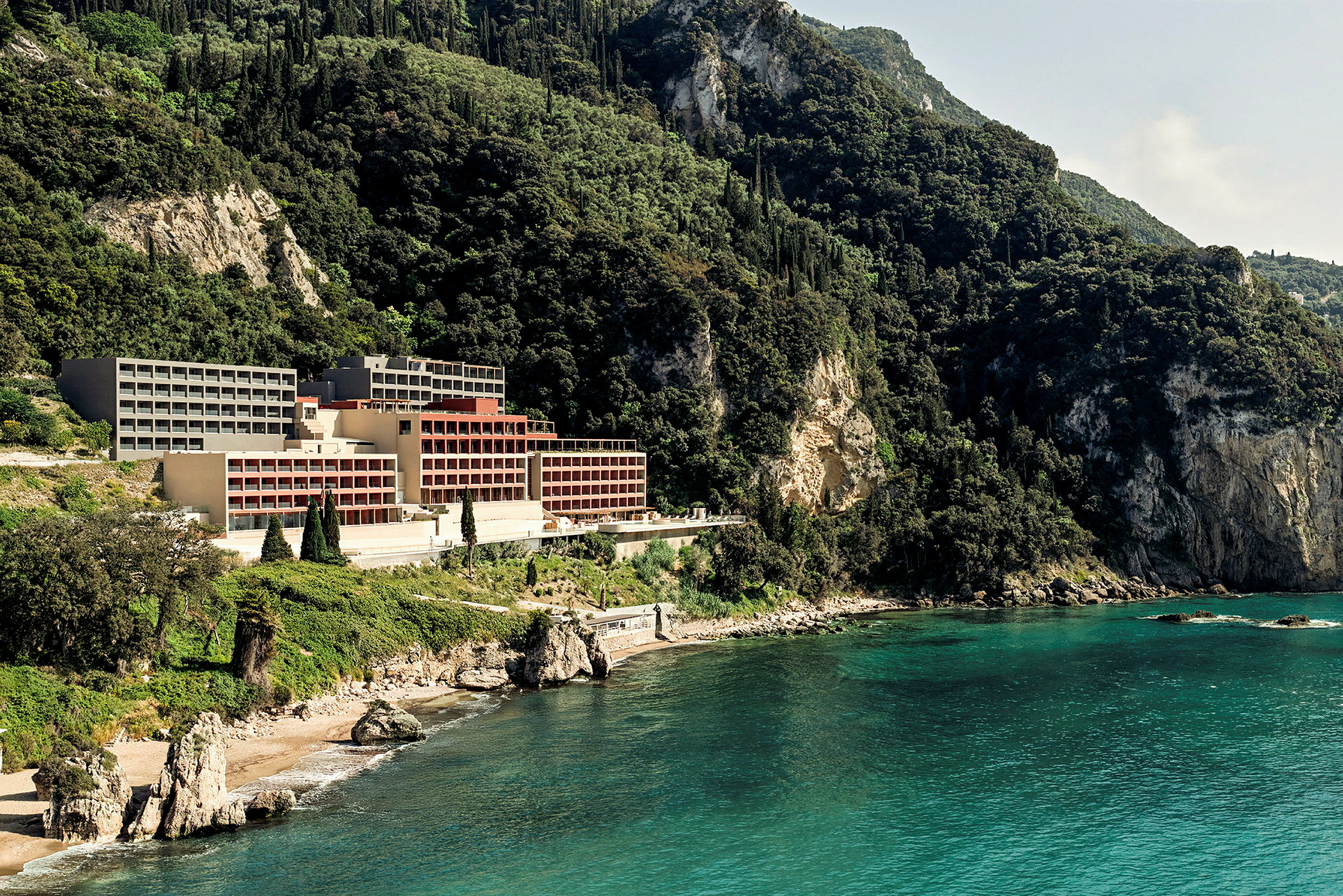 Hotell beläget vid en klippig kust omgiven av grönskande berg. (AI-genererad text)