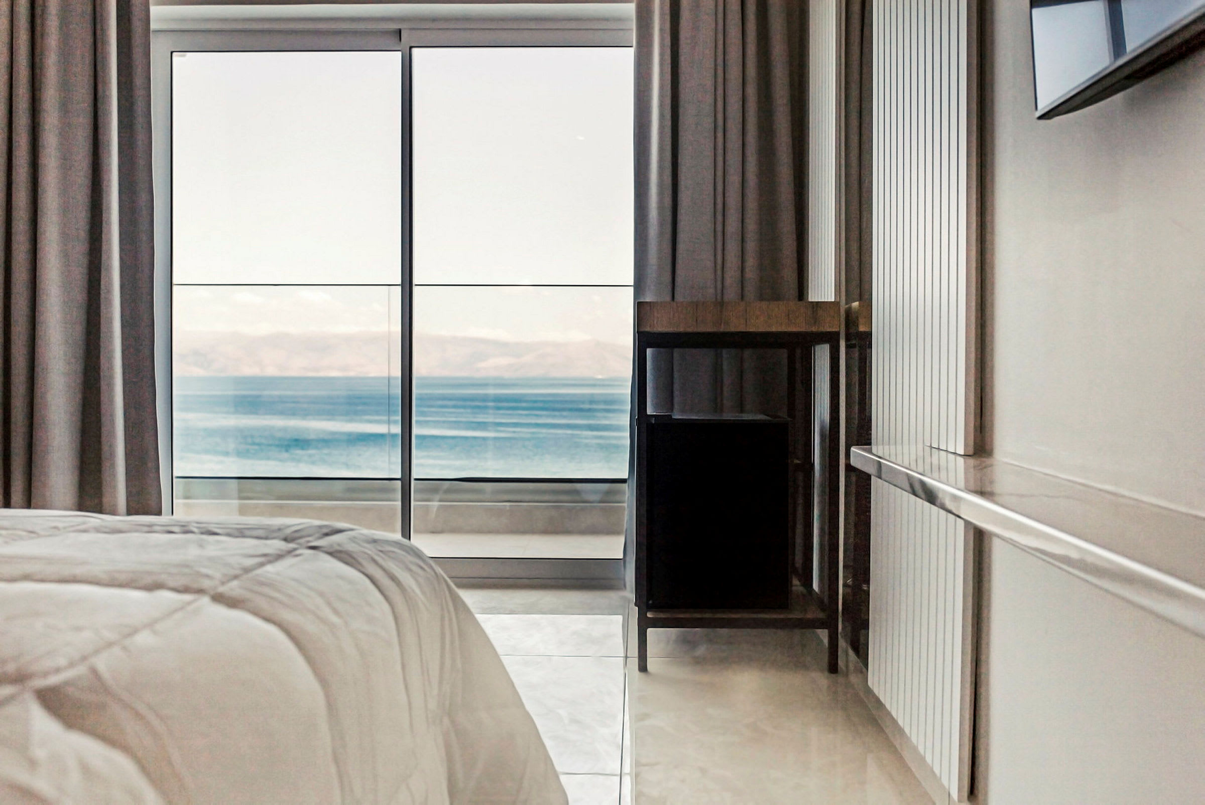 Utsikt från ett hotellrum genom en glasdörr mot ett glittrande hav. (AI-genererad text)