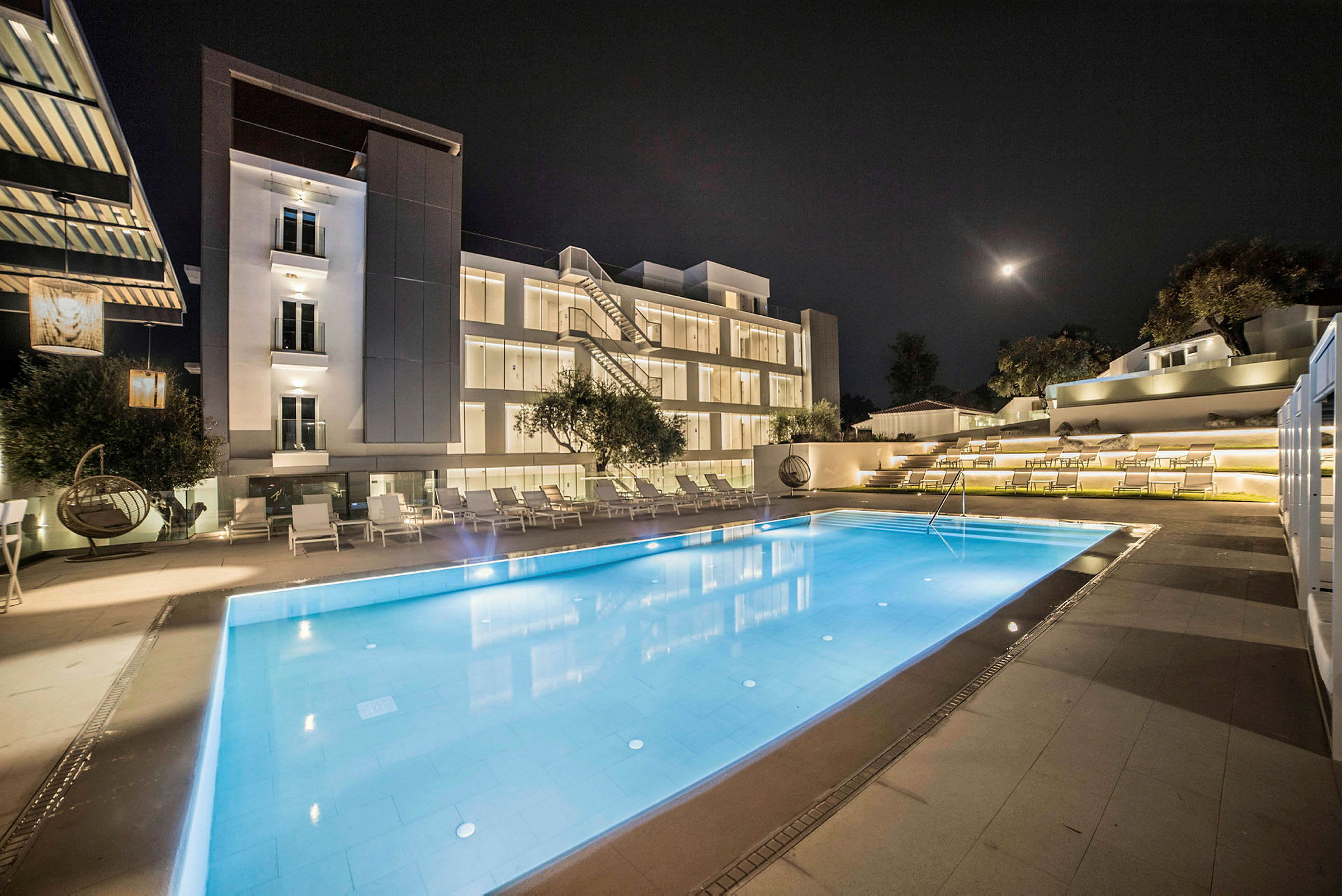Ett hotell med en upplyst swimmingpool framför byggnaden under kvällen. (AI-genererad text)