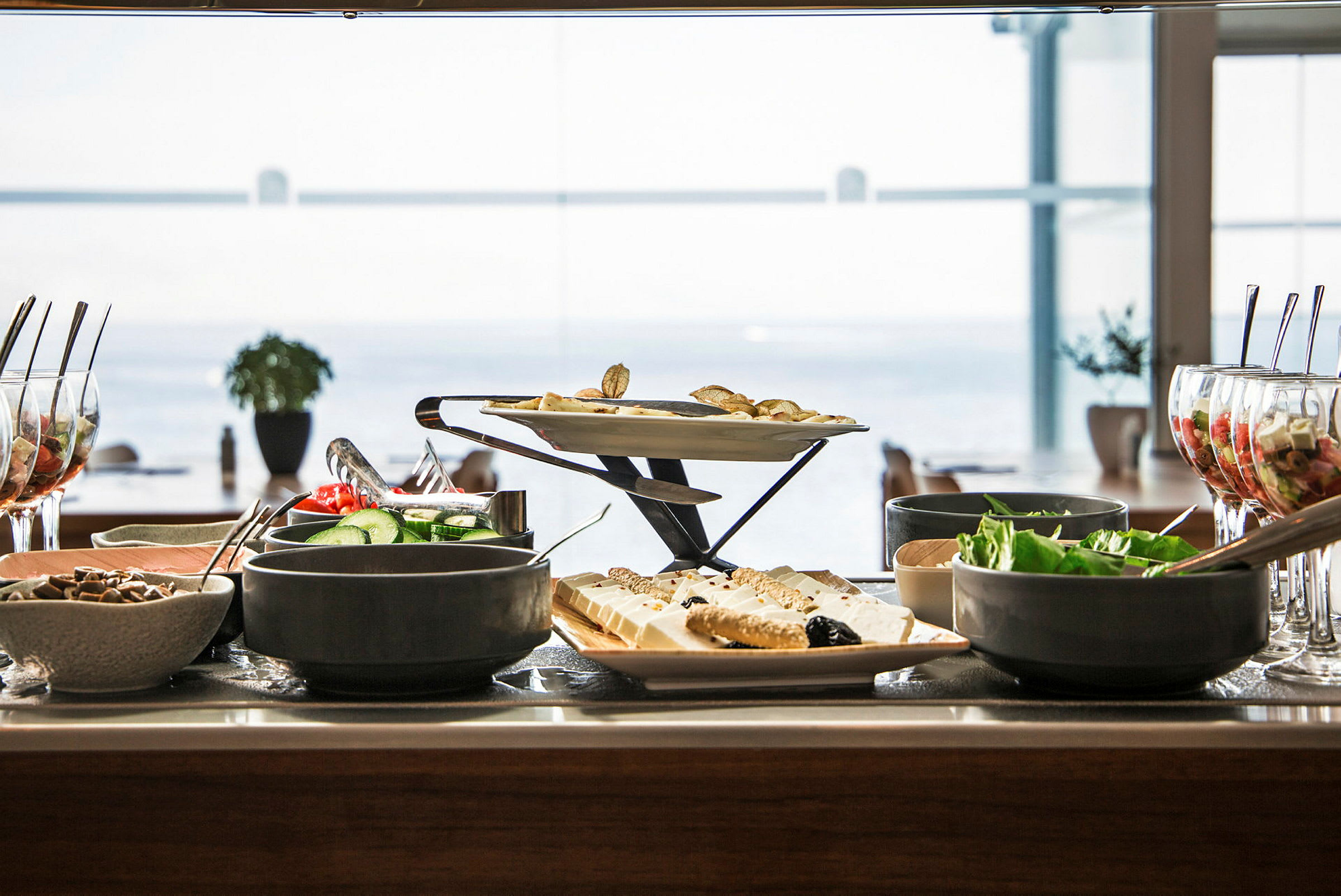 Buffé med olika maträtter, sallader och desserter på ett bord med havsutsikt i bakgrunden. (AI-genererad text)