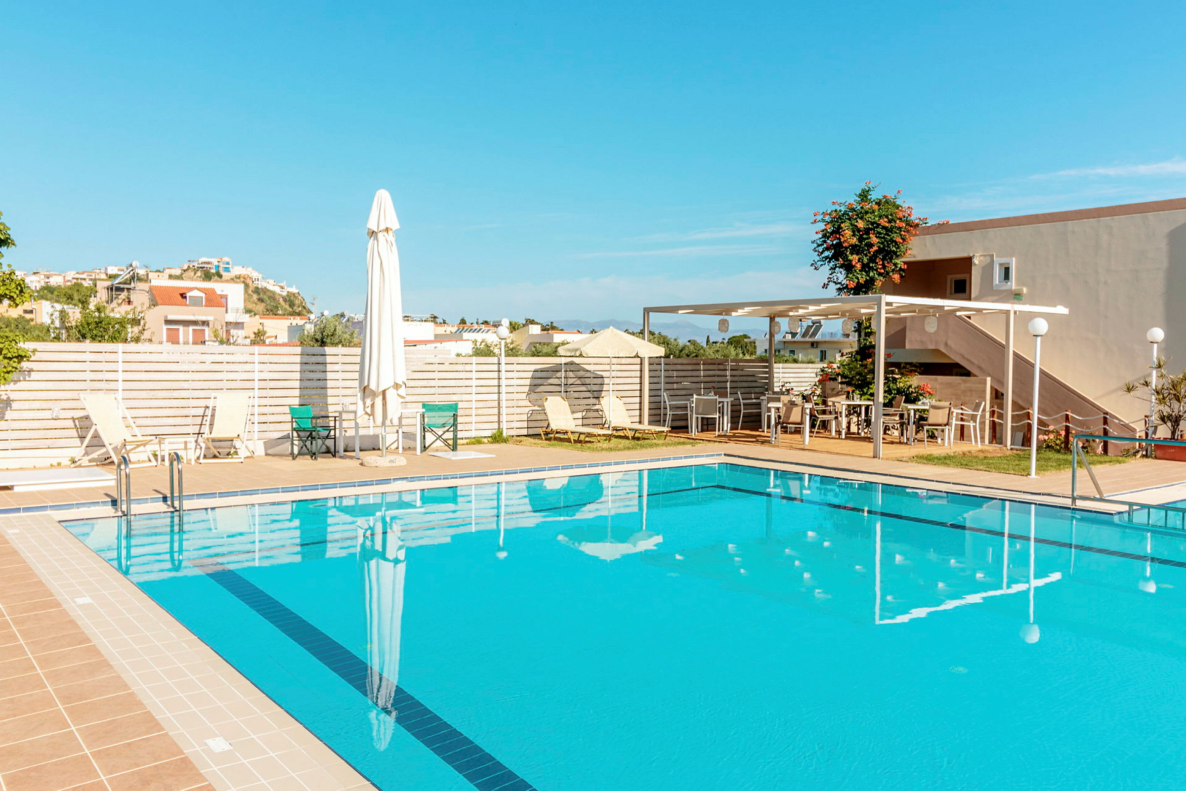 En pool utomhus med solstolar, parasoller och en terrass med bord och stolar. (AI-genererad text)