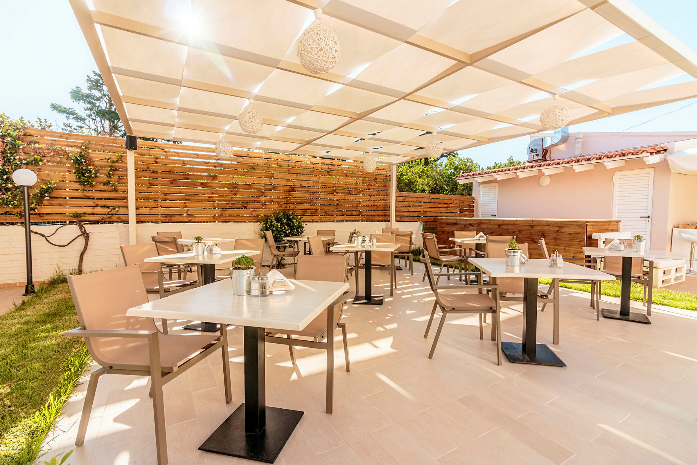 En utomhusterrass med bord och stolar under ett skuggande tak. (AI-genererad text)