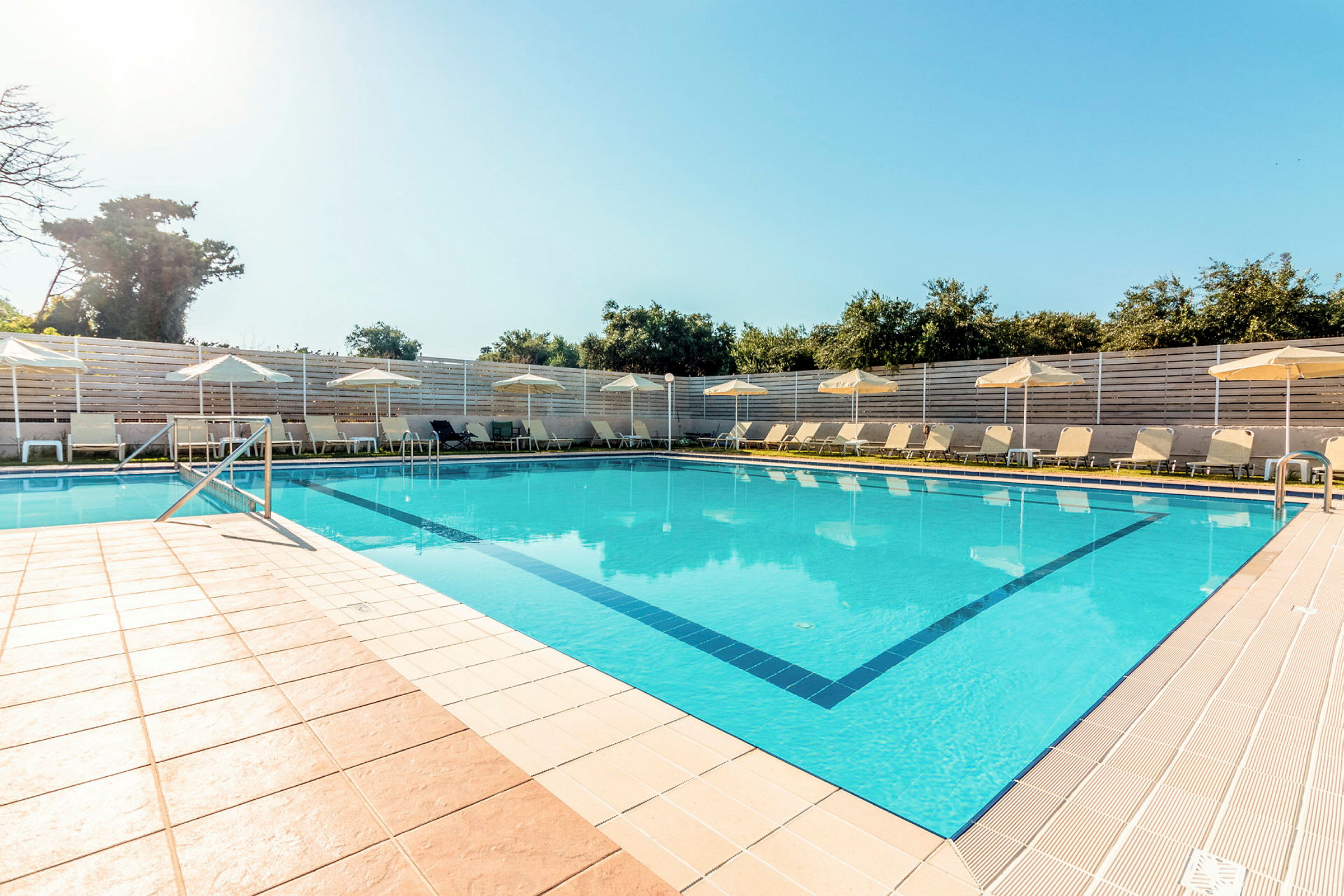 En pool omgiven av solstolar och parasoll under en klarblå himmel. (AI-genererad text)