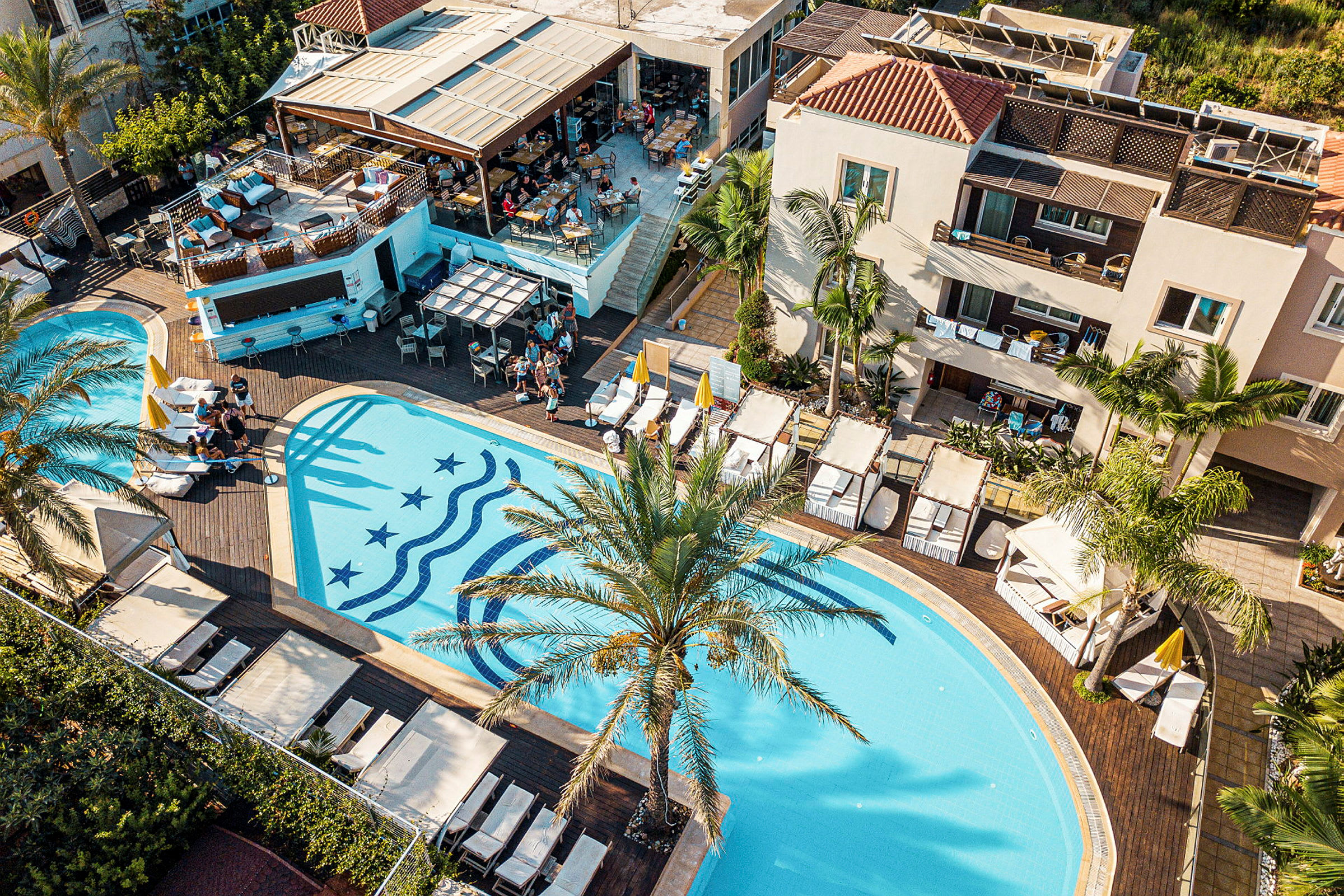 Flygvy över en pool vid ett hotellområde med solstolar och en omgivande trädgård. (AI-genererad text)