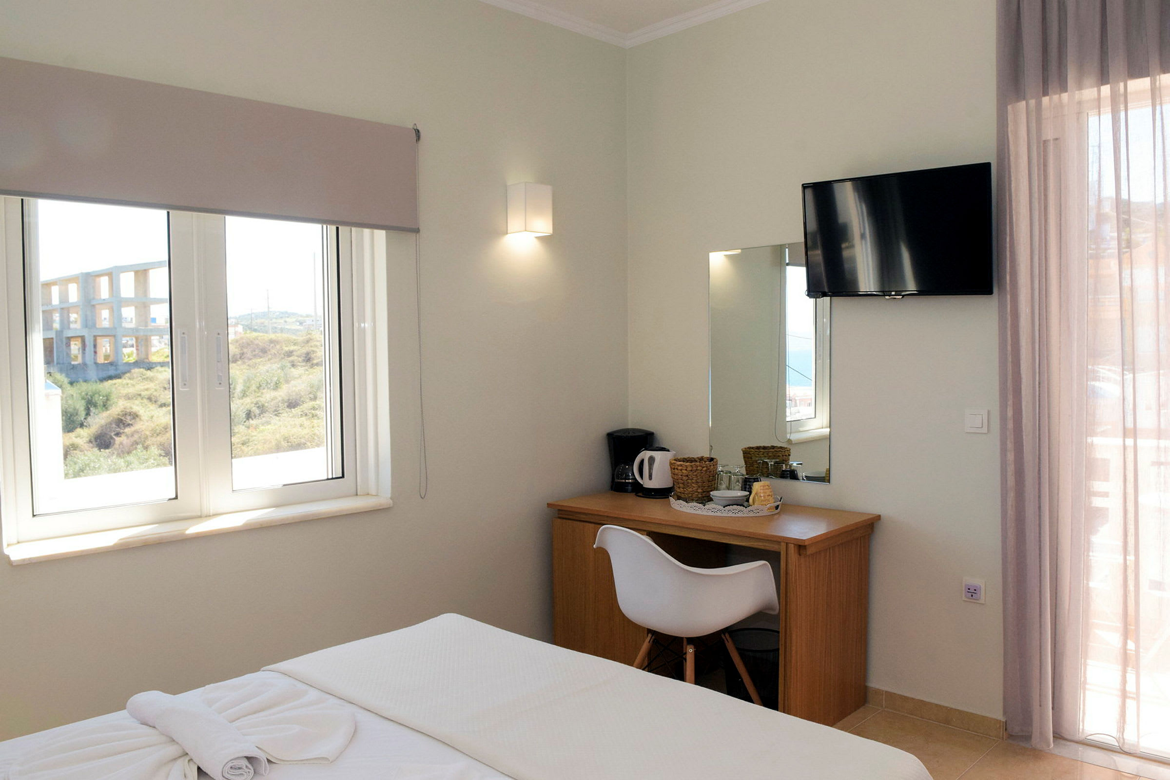 Bild av ett hotellrum med en säng, fönster med utsikt, skrivbord med spegel och en väggmonterad TV. (AI-genererad text)