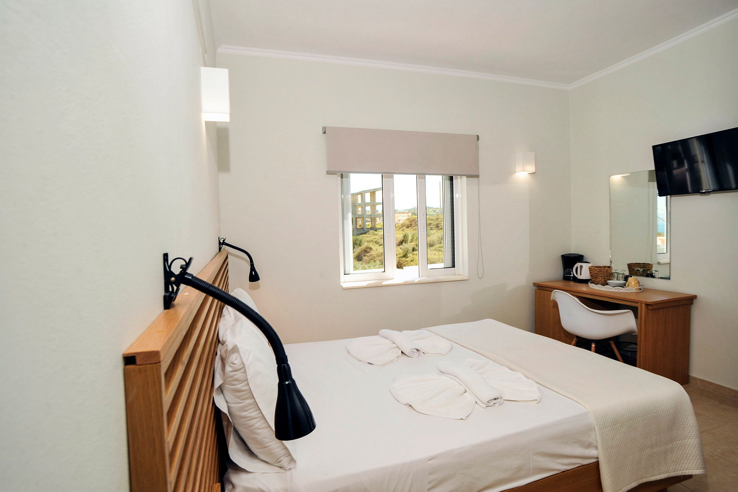 Ett hotellrum med en säng, fönster, skrivbord, stol och TV. (AI-genererad text)