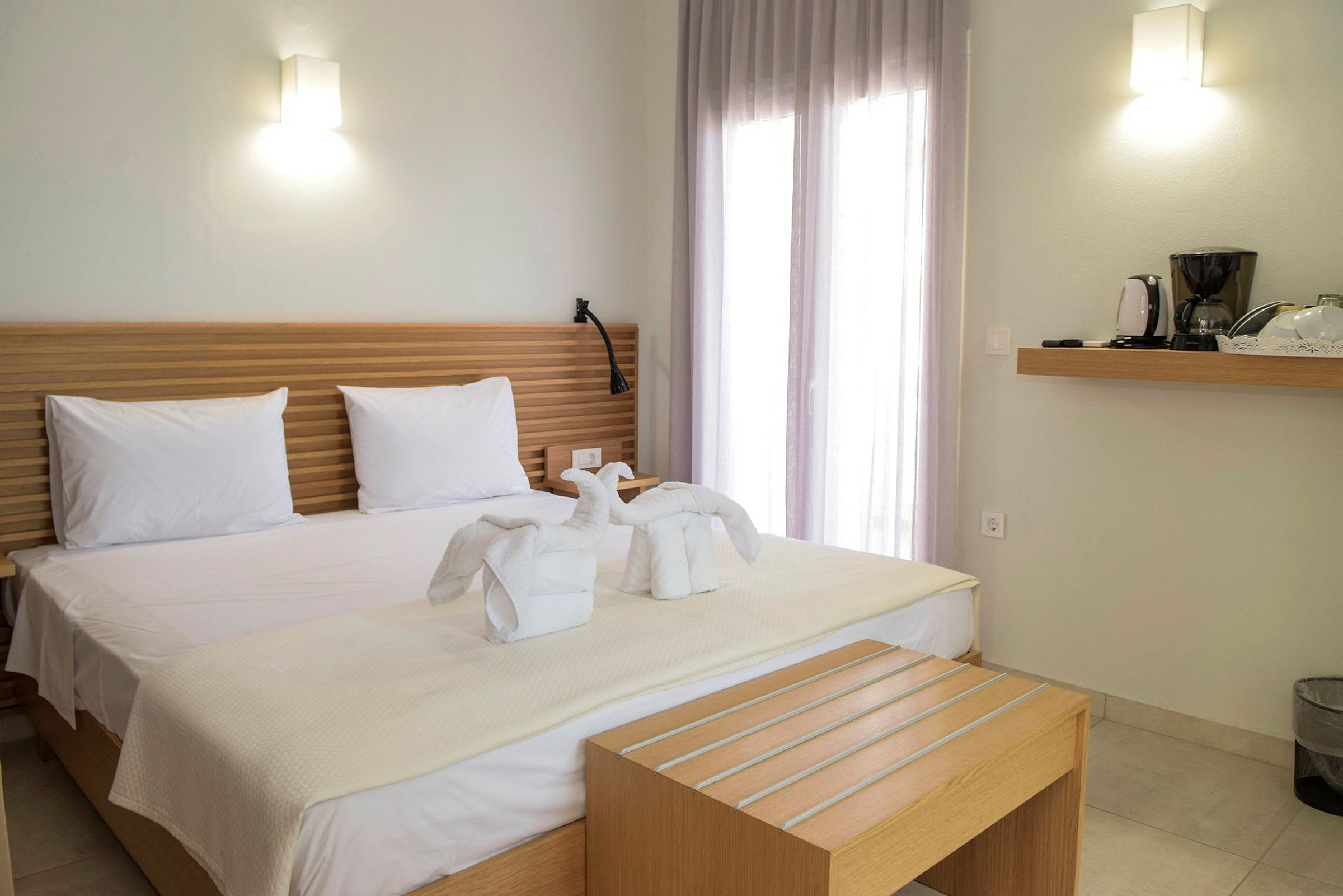 Hotellrum med en dubbelsäng med vita lakan och svanformade handdukar, samt en hylla med kaffebryggare. (AI-genererad text)