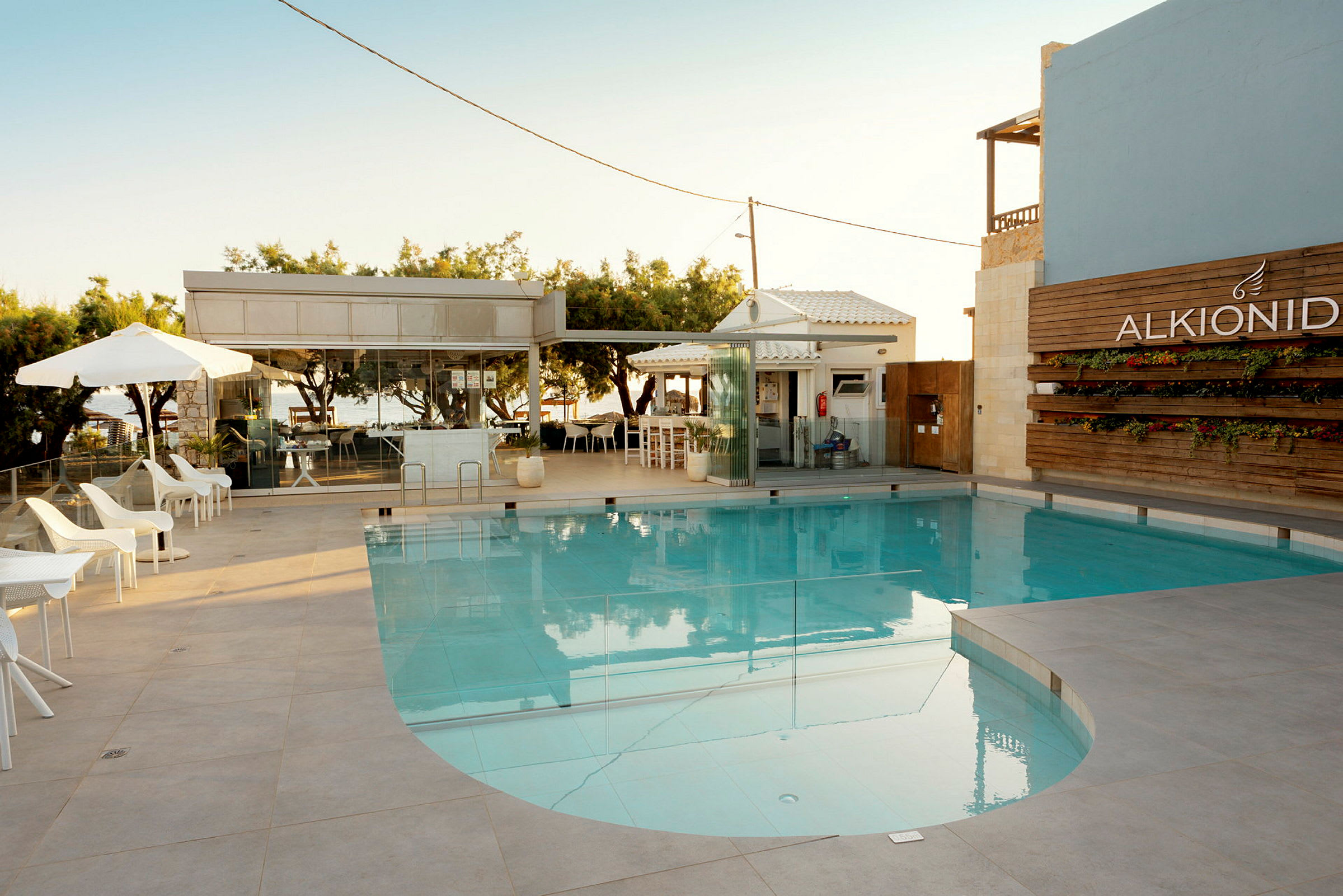 En pool med solsängar och parasoll intill, samt en byggnad i bakgrunden. (AI-genererad text)