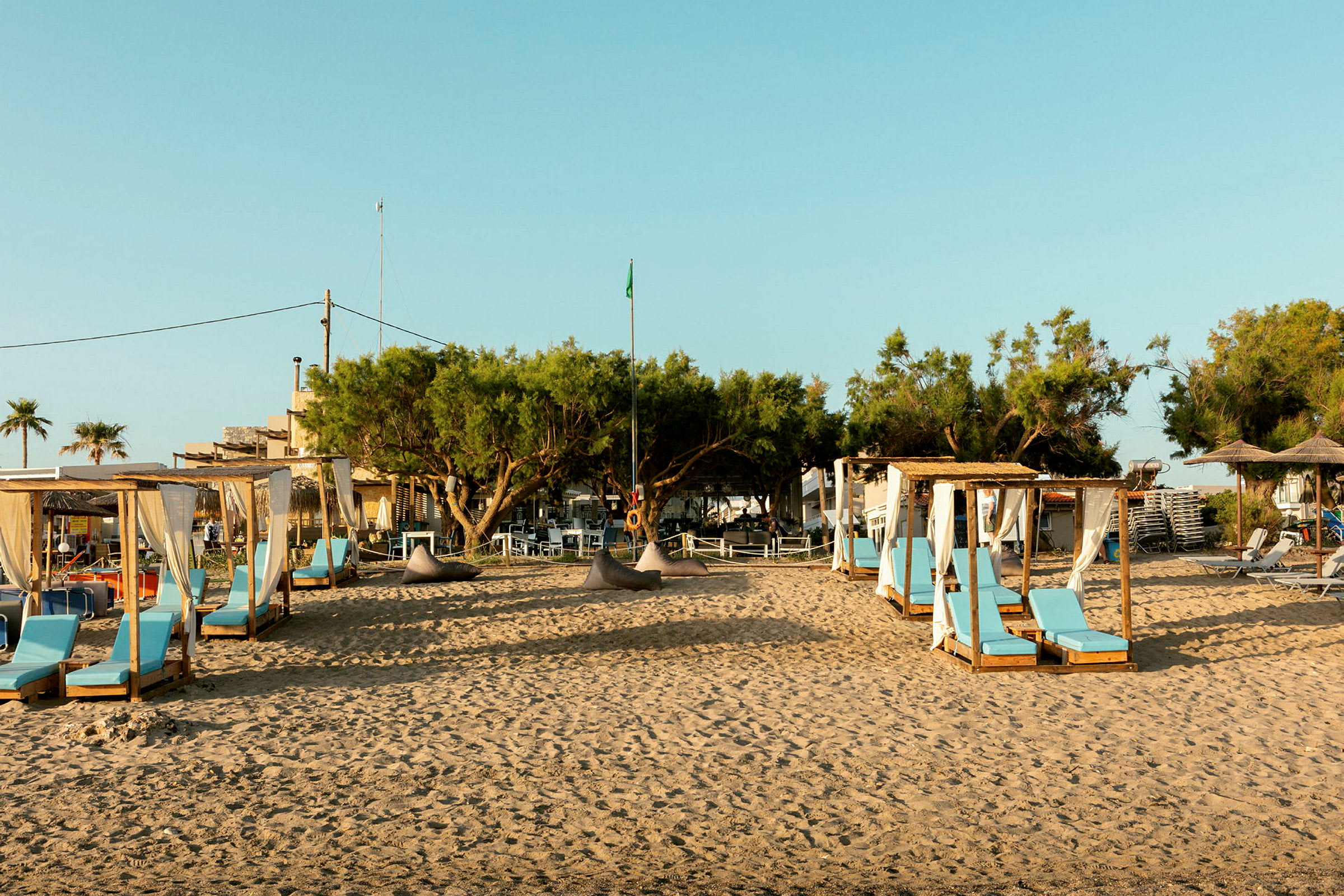 En sandstrand med solstolar och små paviljonger omgivna av träd. (AI-genererad text)