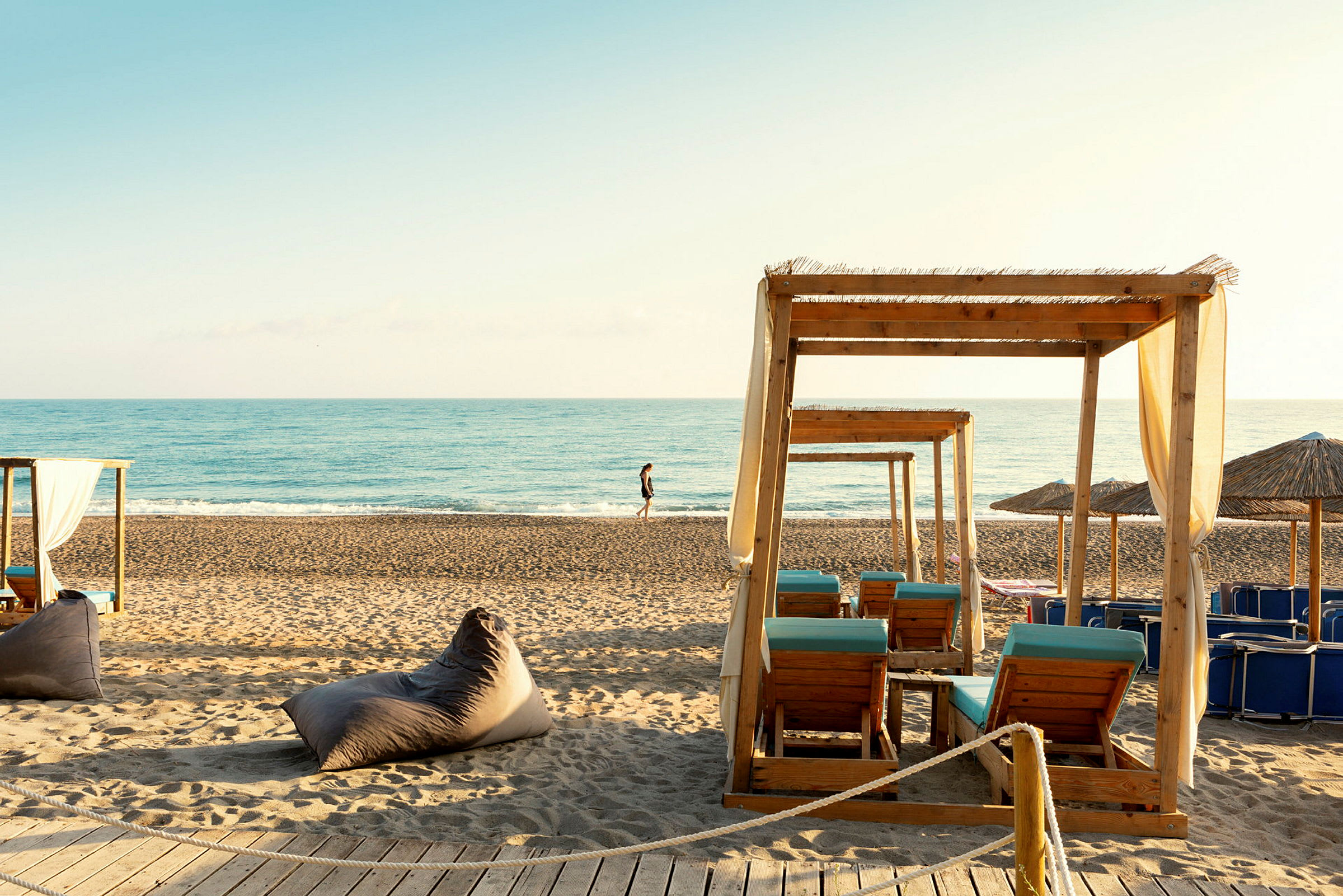 Strand med solstolar under träpergolas, hav i bakgrunden. (AI-genererad text)