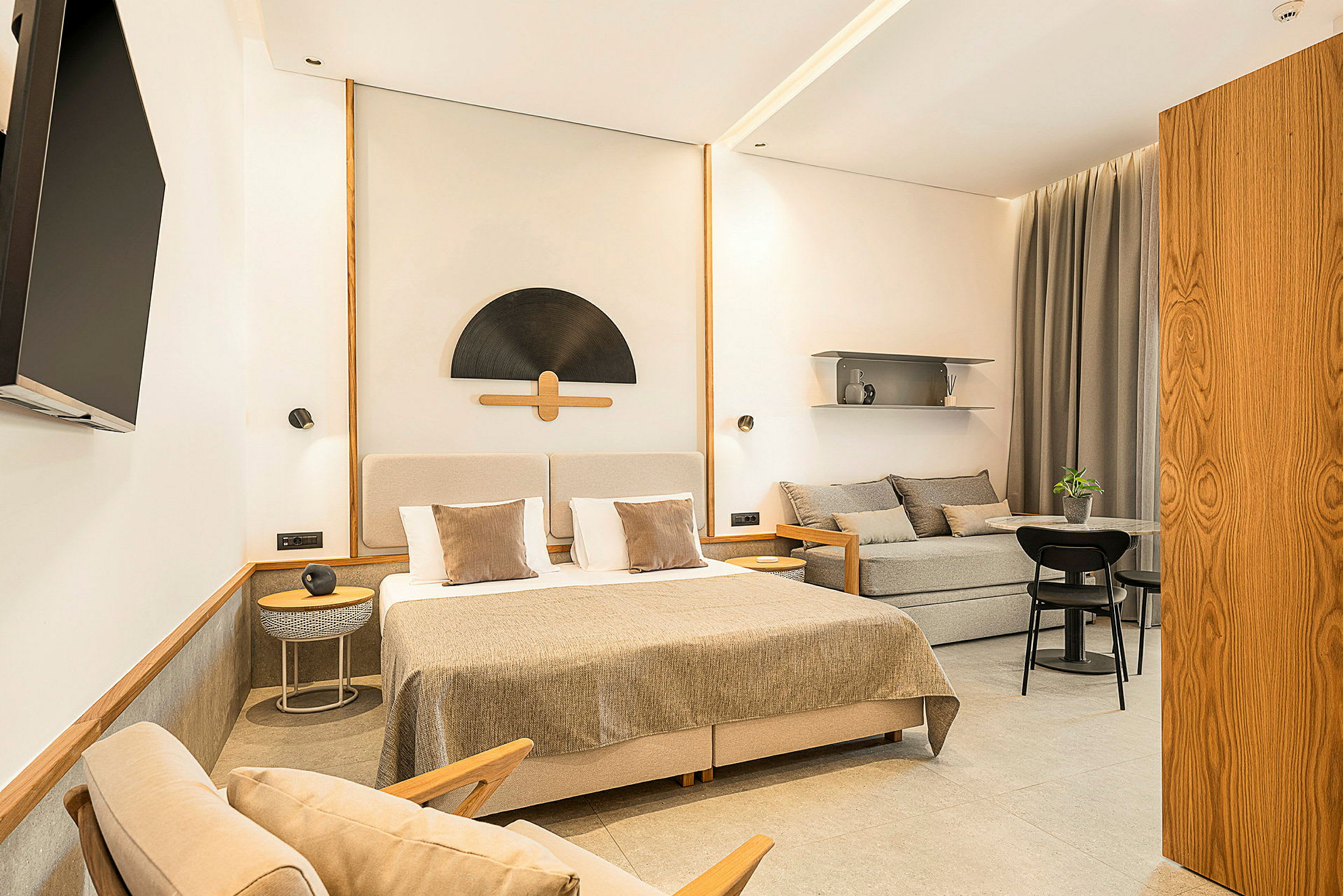 Ett stilrent hotellrum med en dubbelsäng, soffa, bord och en väggmonterad TV. (AI-genererad text)