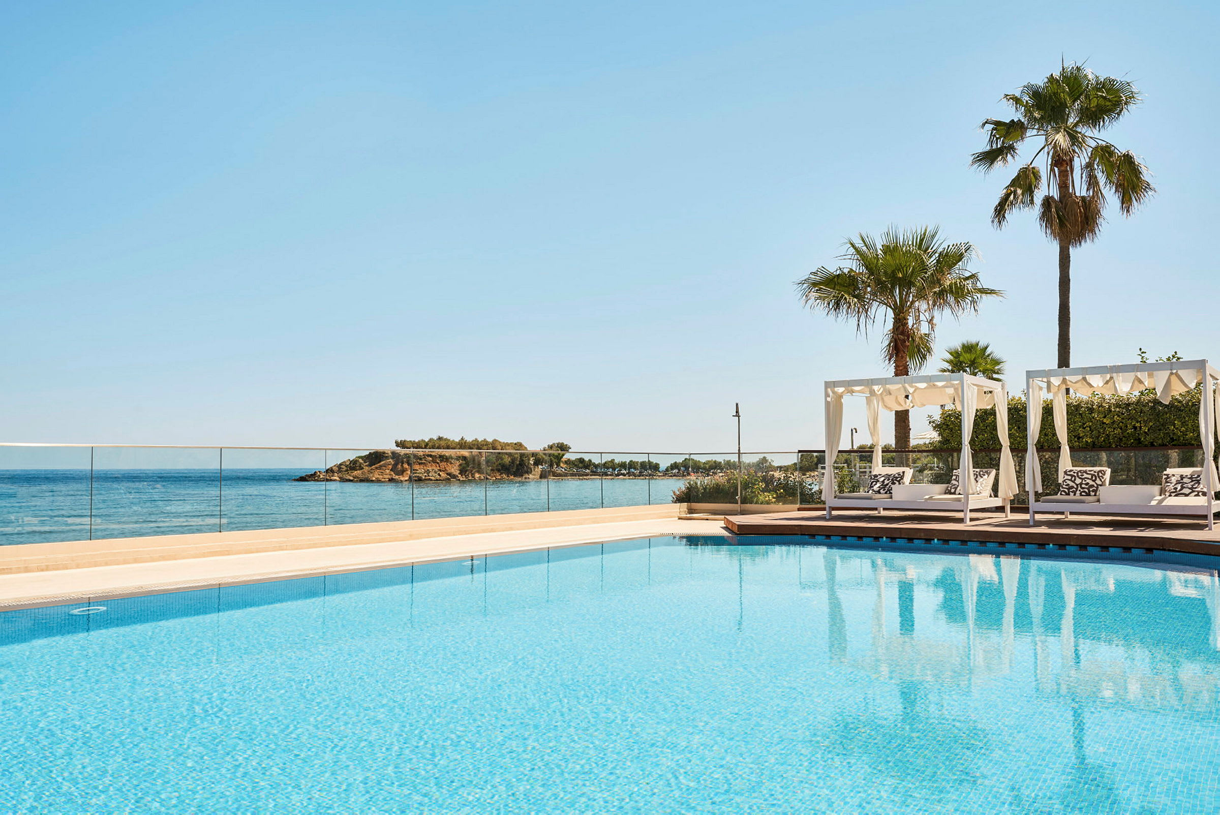 Utomhuspool med utsikt över havet och solstolar under pergola. (AI-genererad text)
