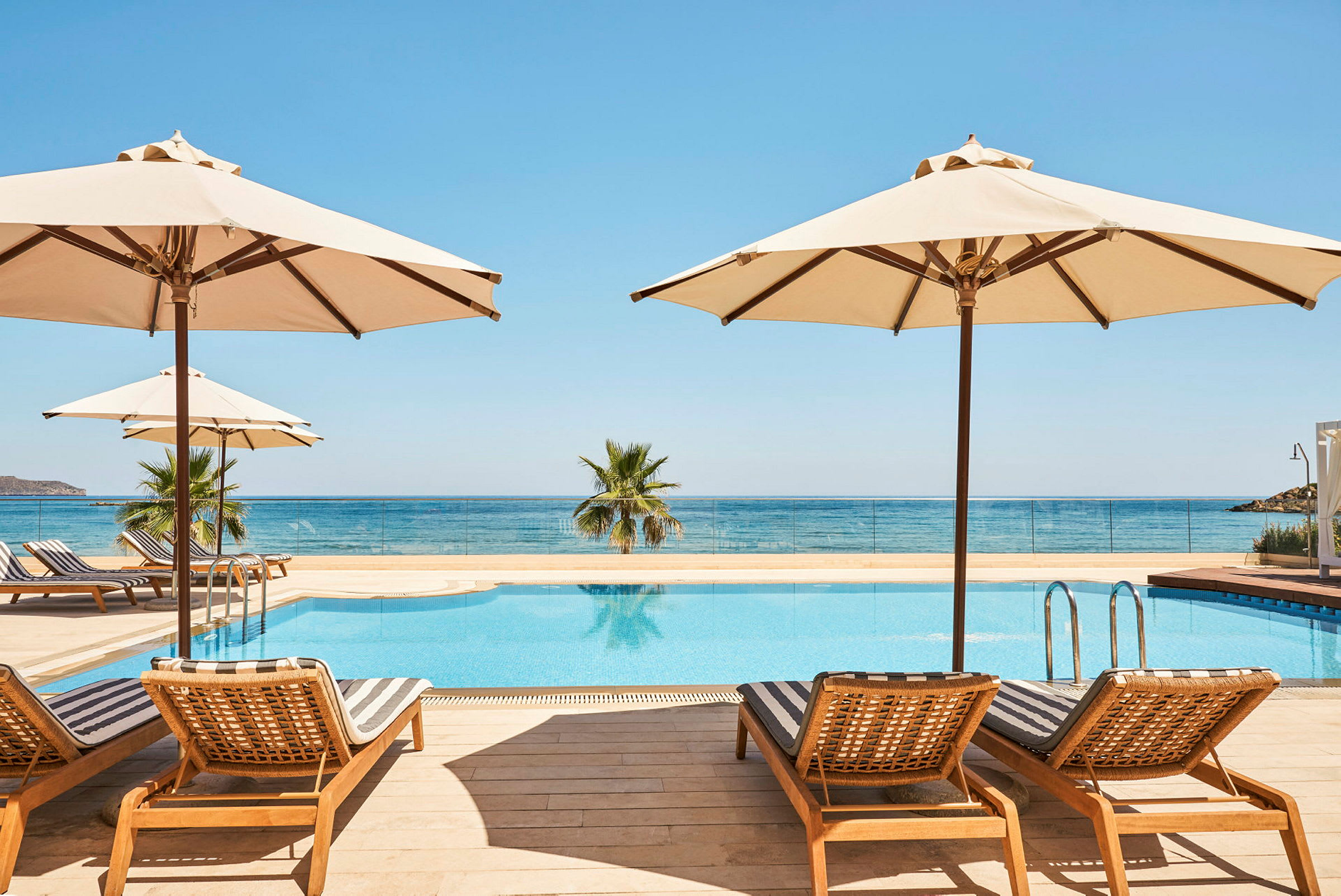 Bild av solstolar och parasoller vid en pool nära havet. (AI-genererad text)