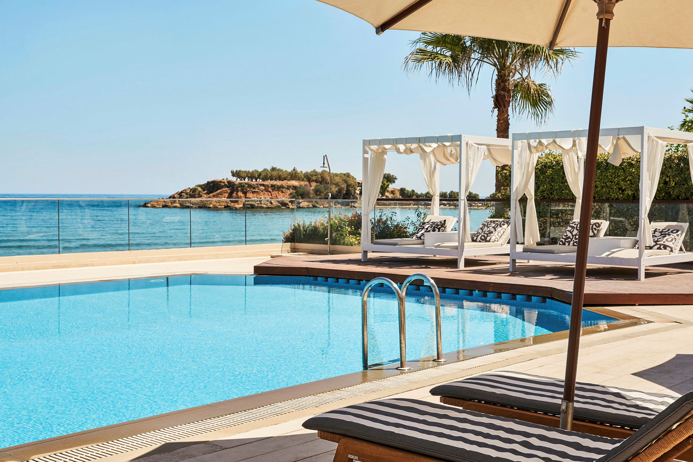 En pool med solstolar och baldakinsängar, med utsikt över havet. (AI-genererad text)