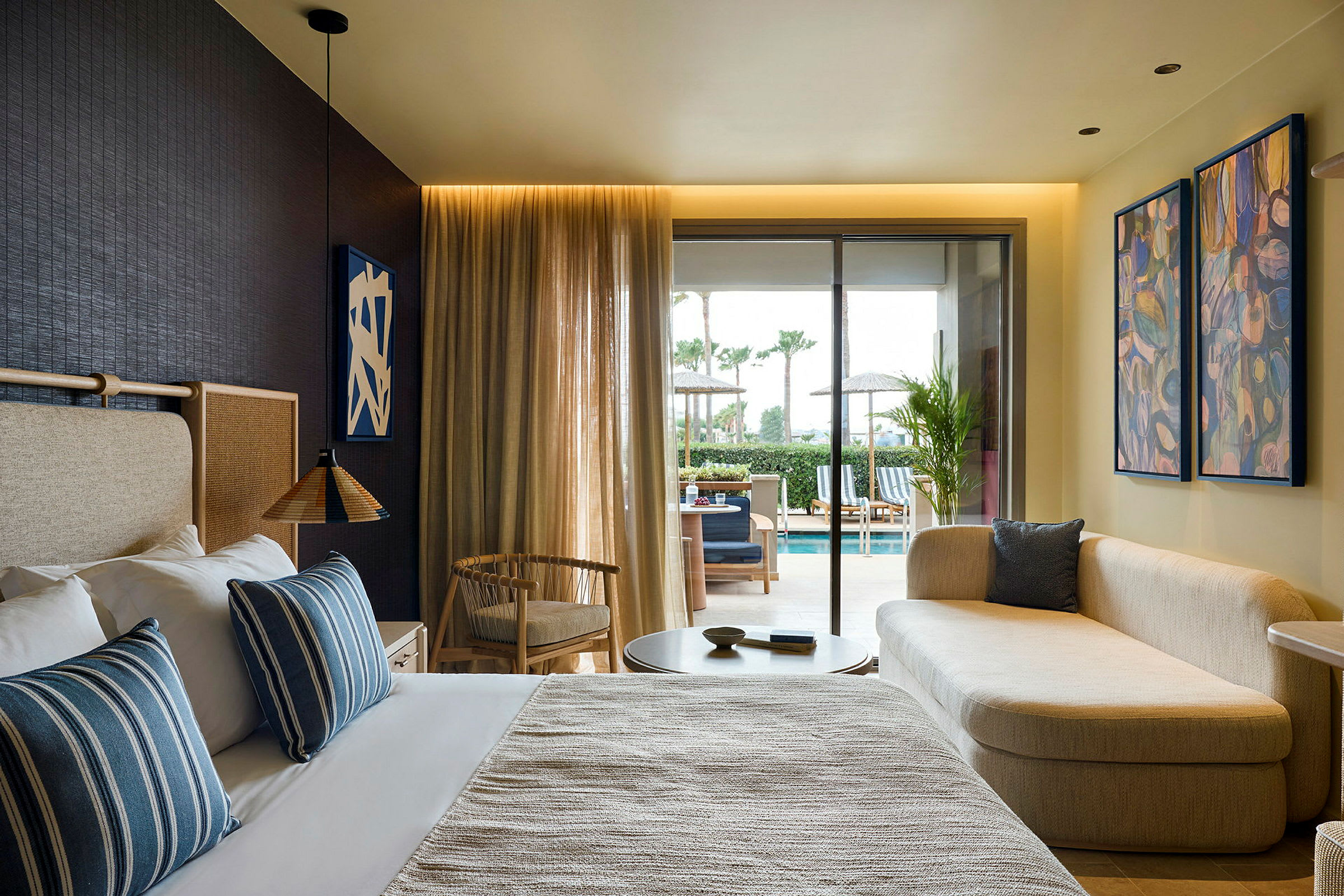 Ett rum med säng, soffa och utsikt mot en terrass med pool. (AI-genererad text)