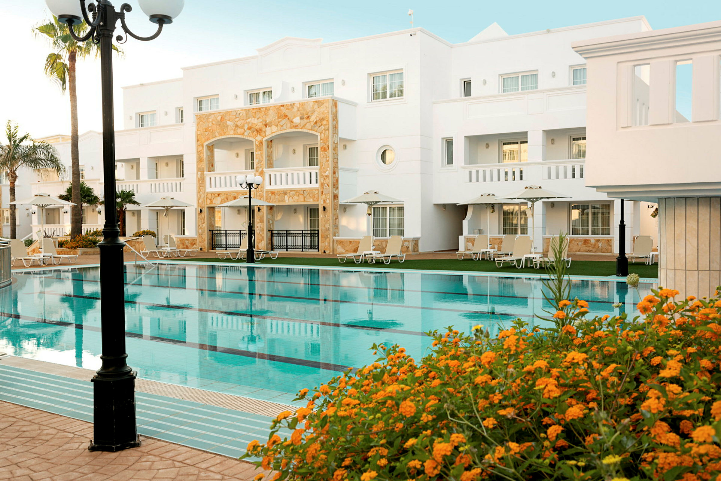 Hotellbyggnad med pool och omgivande solsängar. (AI-genererad text)