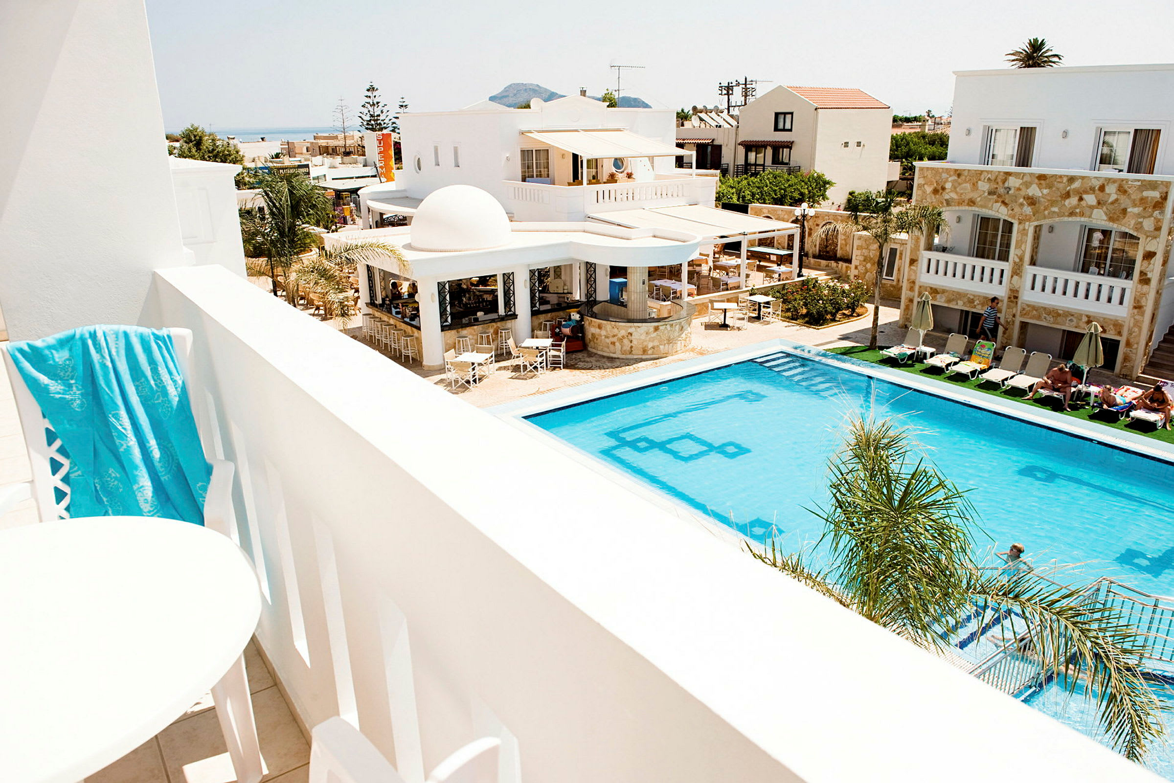 Utsikt från en balkong över en pool och hotellbyggnader. (AI-genererad text)