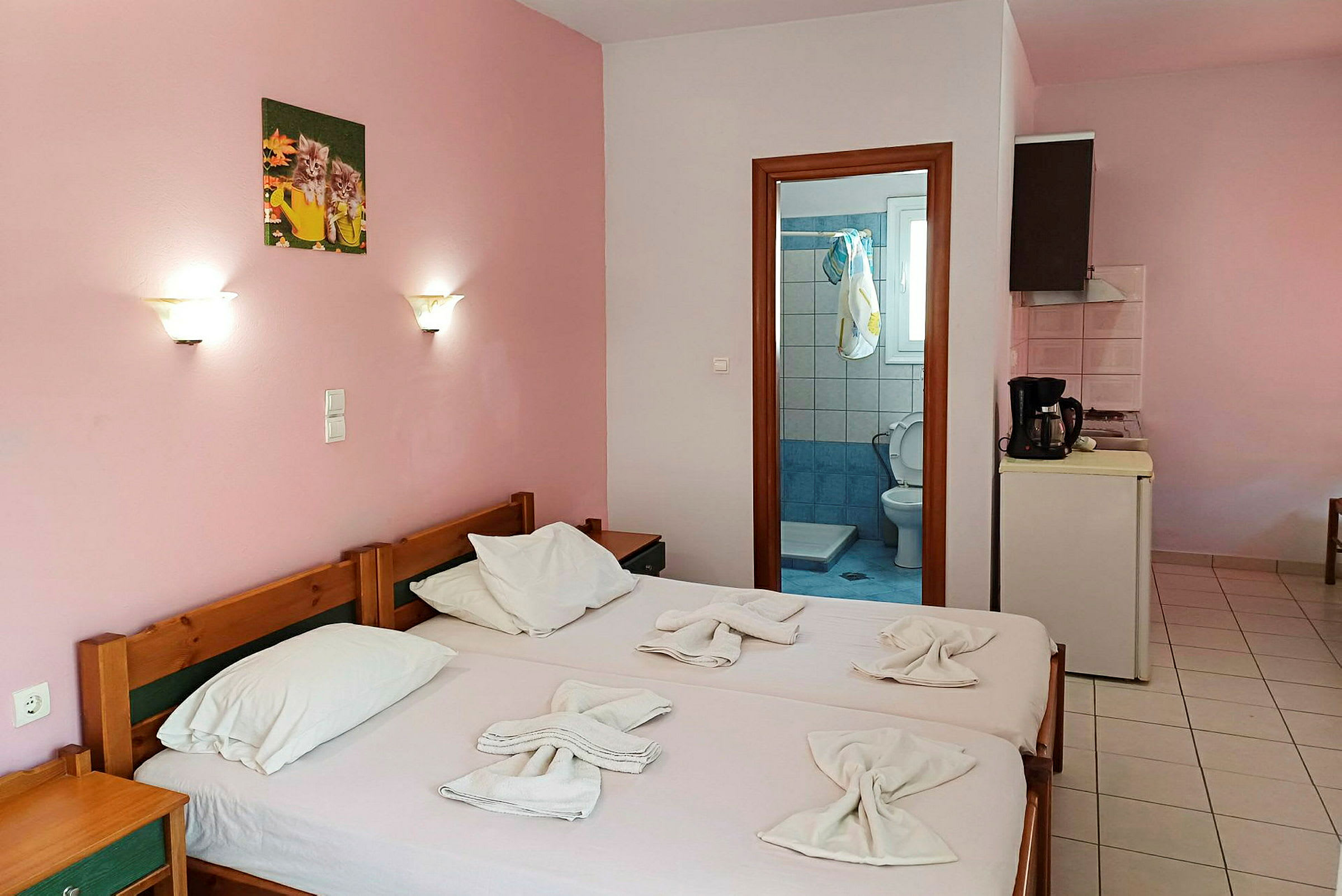 Ett enklare hotellrum med rosa väggar, två enkelsängar och utsikt mot badrumsdörren. (AI-genererad text)
