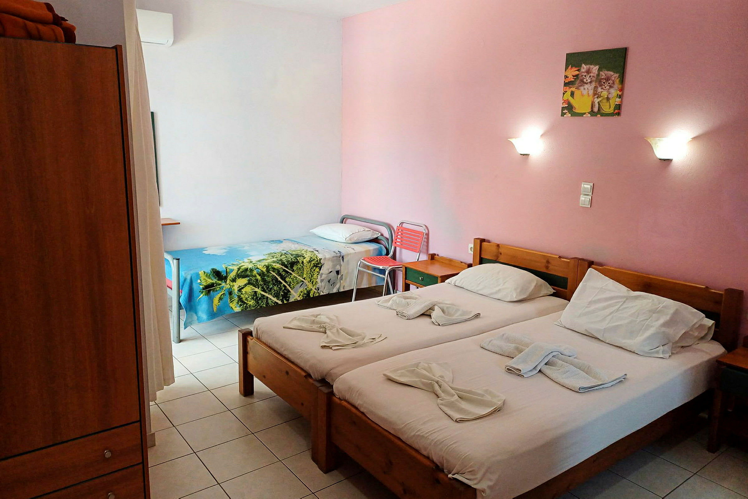 Bild på ett hotellrum med två enkelbäddar och en enkelsäng, rosa väggar och vägglampor. (AI-genererad text)