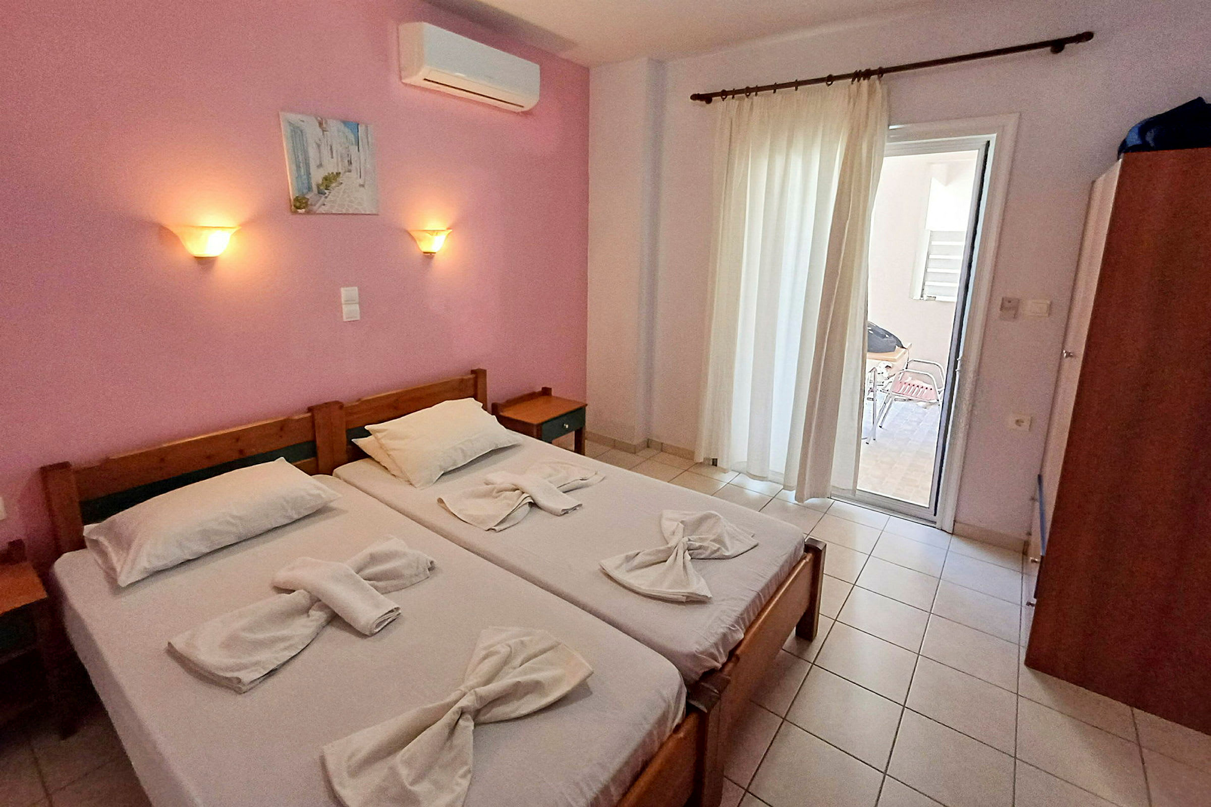Två enkelsängar med vita sängkläder i ett rum med rosa väggar och ett glasdörr som leder ut till en balkong. (AI-genererad text)