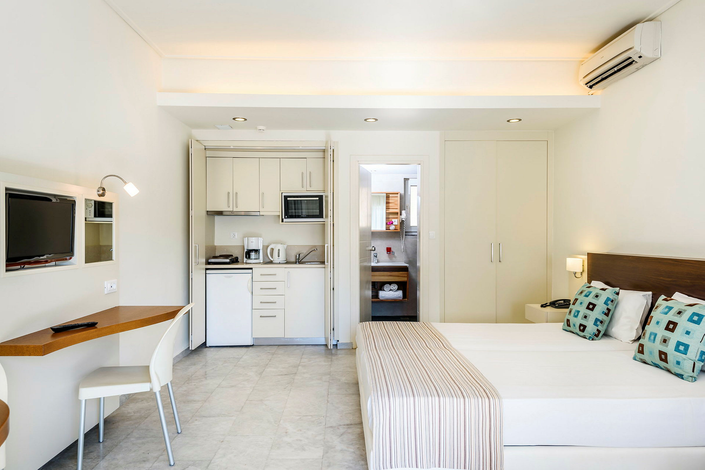 Ett hotellrum med en köksdel, skrivbord, säng och badrum. (AI-genererad text)