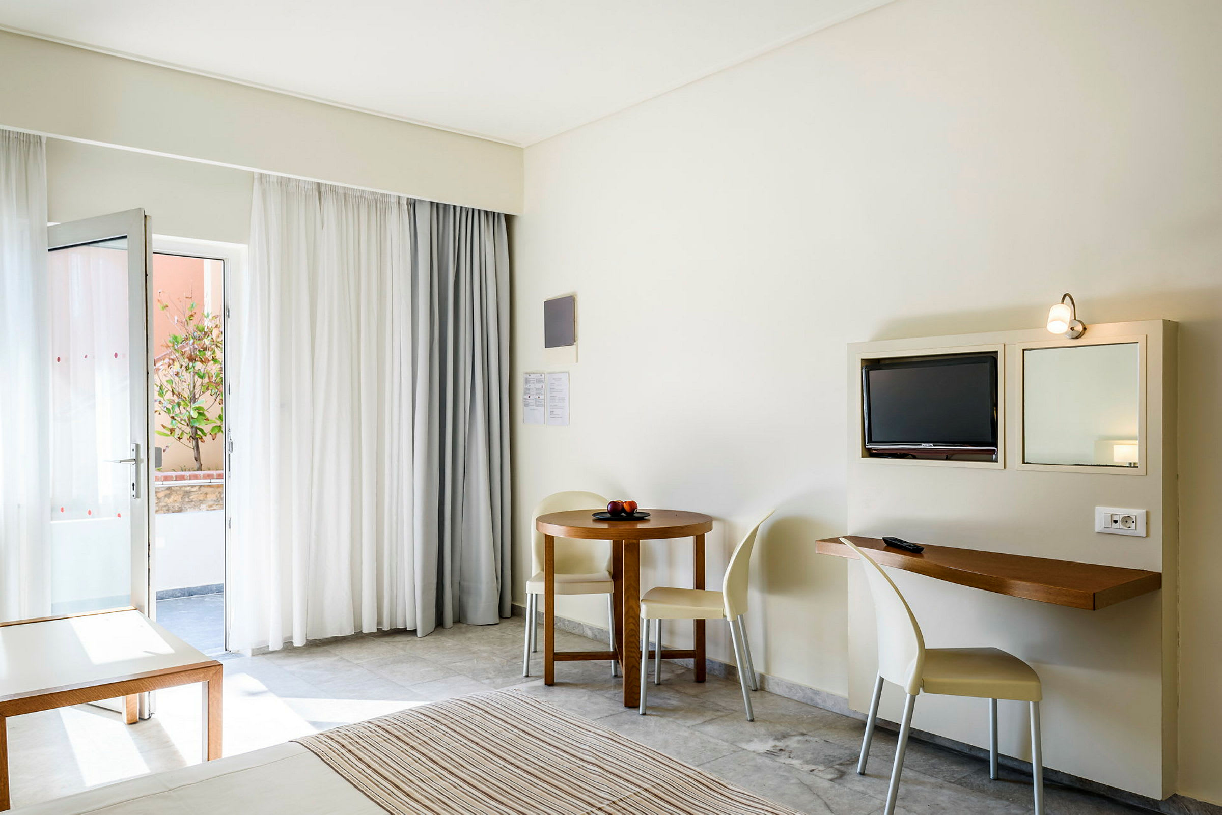 Ett hotellrum med en öppen dörr, en liten matplats, och en tv monterad på väggen. (AI-genererad text)