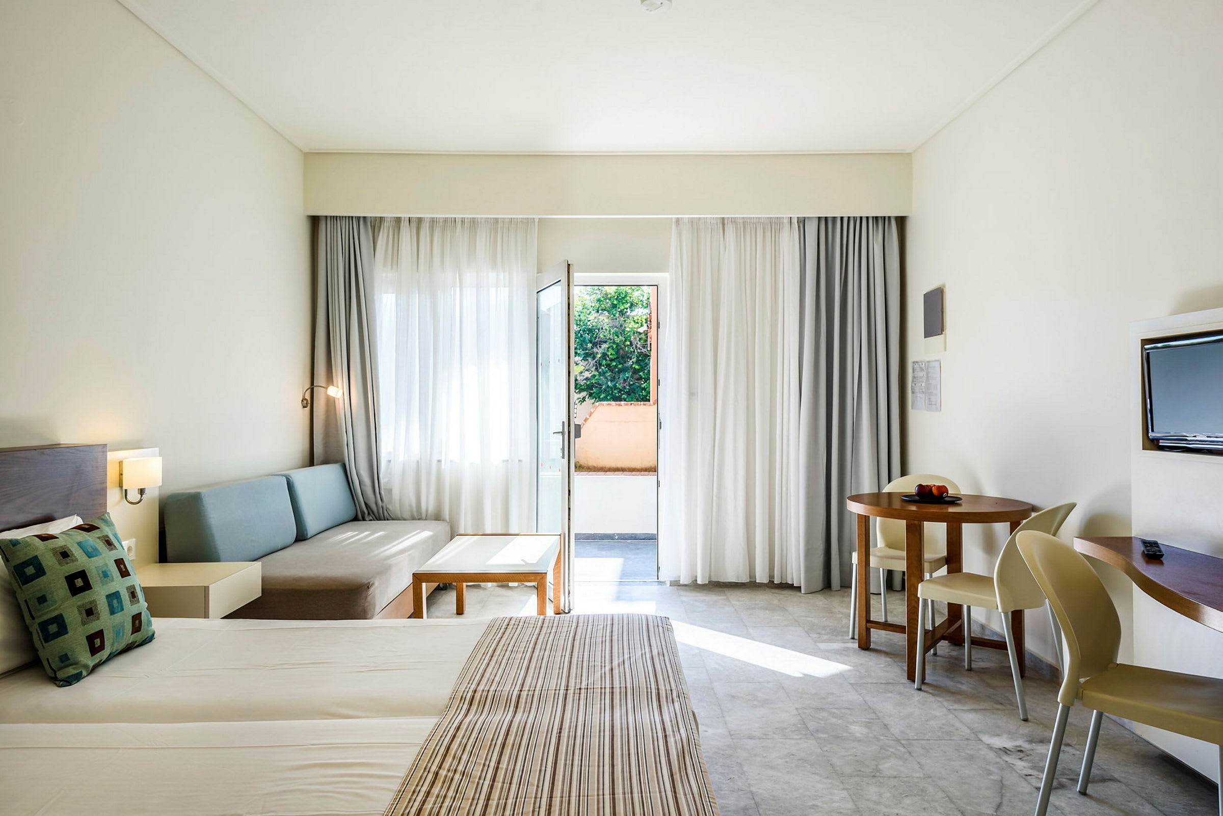 Hotellrum med bäddad säng, sittgrupp, rund matbord och balkongdörr. (AI-genererad text)