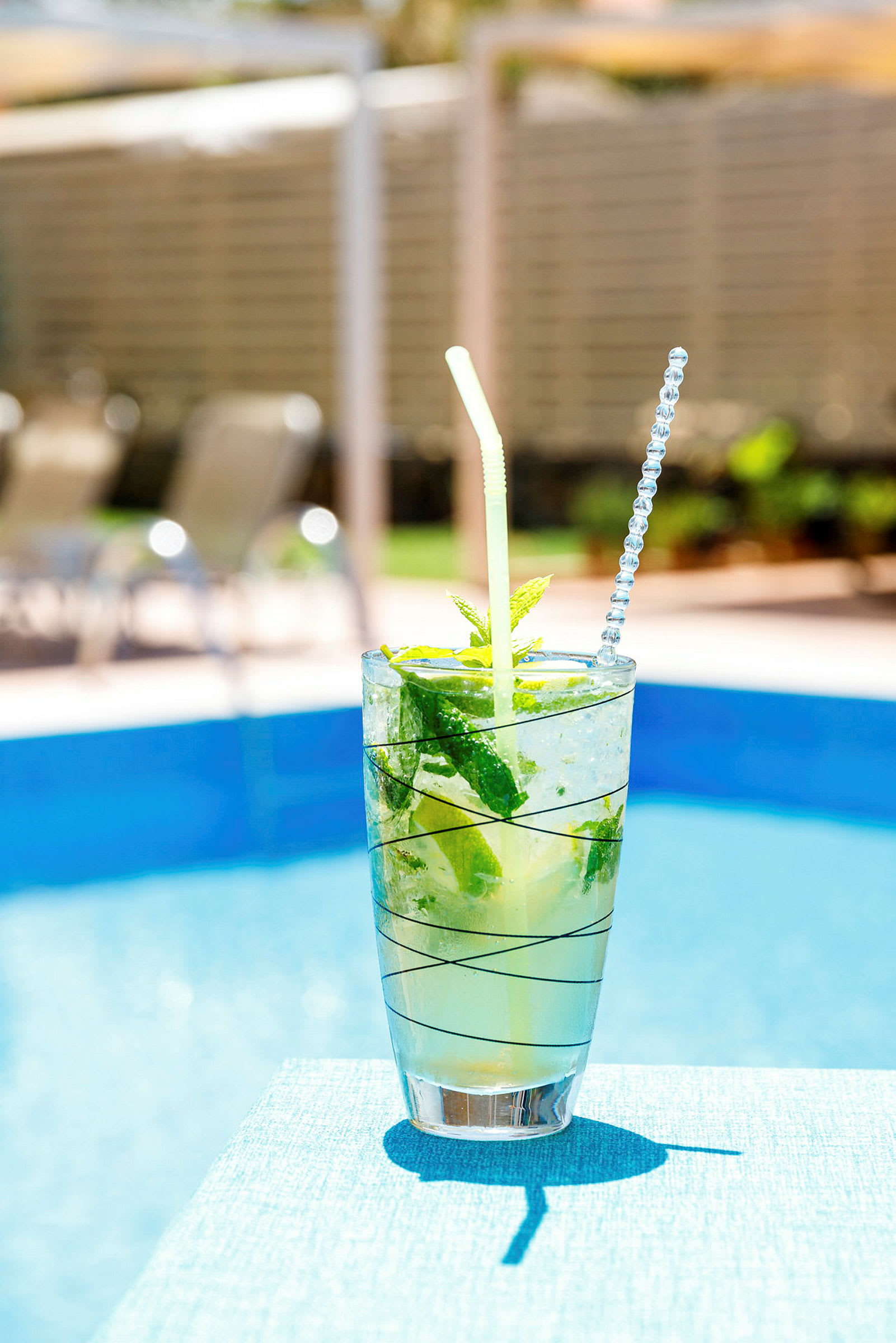 En glasdrink med is, mynta och lime vid en pool. (AI-genererad text)