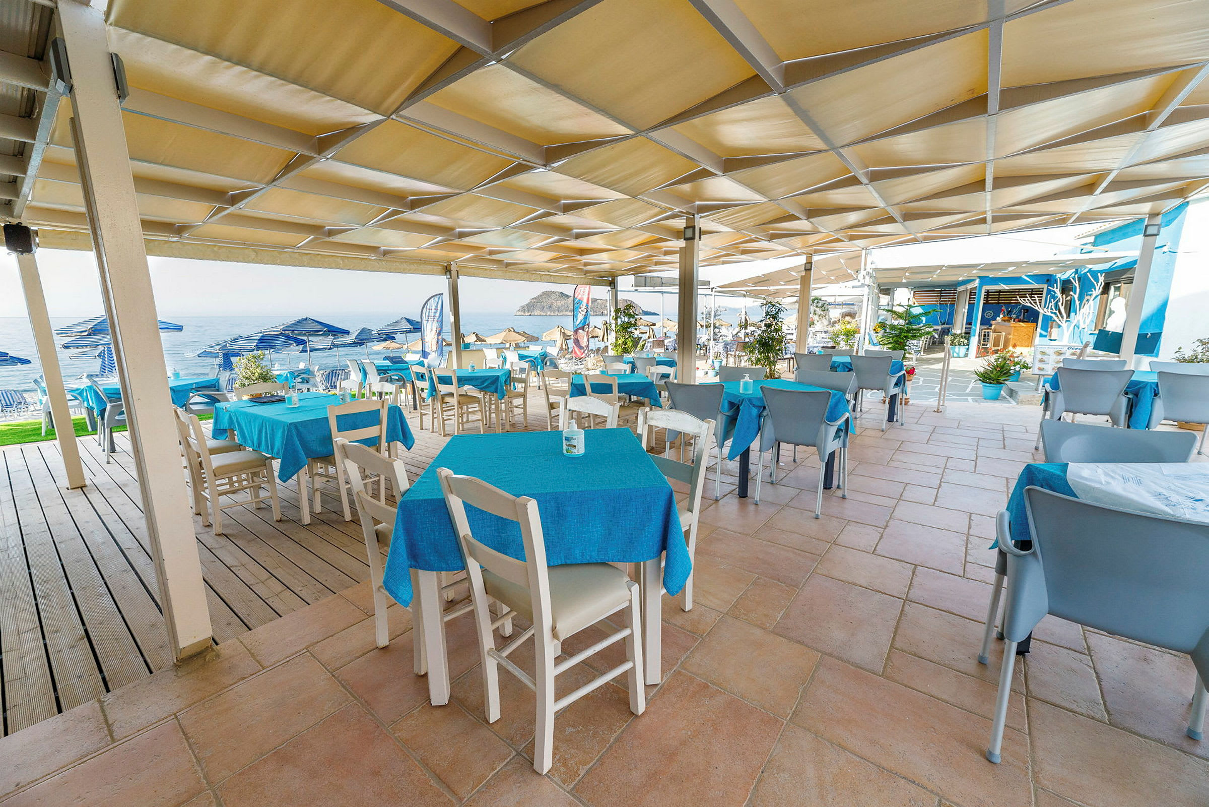 Utomhusrestaurang med blå dukar och utsikt mot havet. (AI-genererad text)