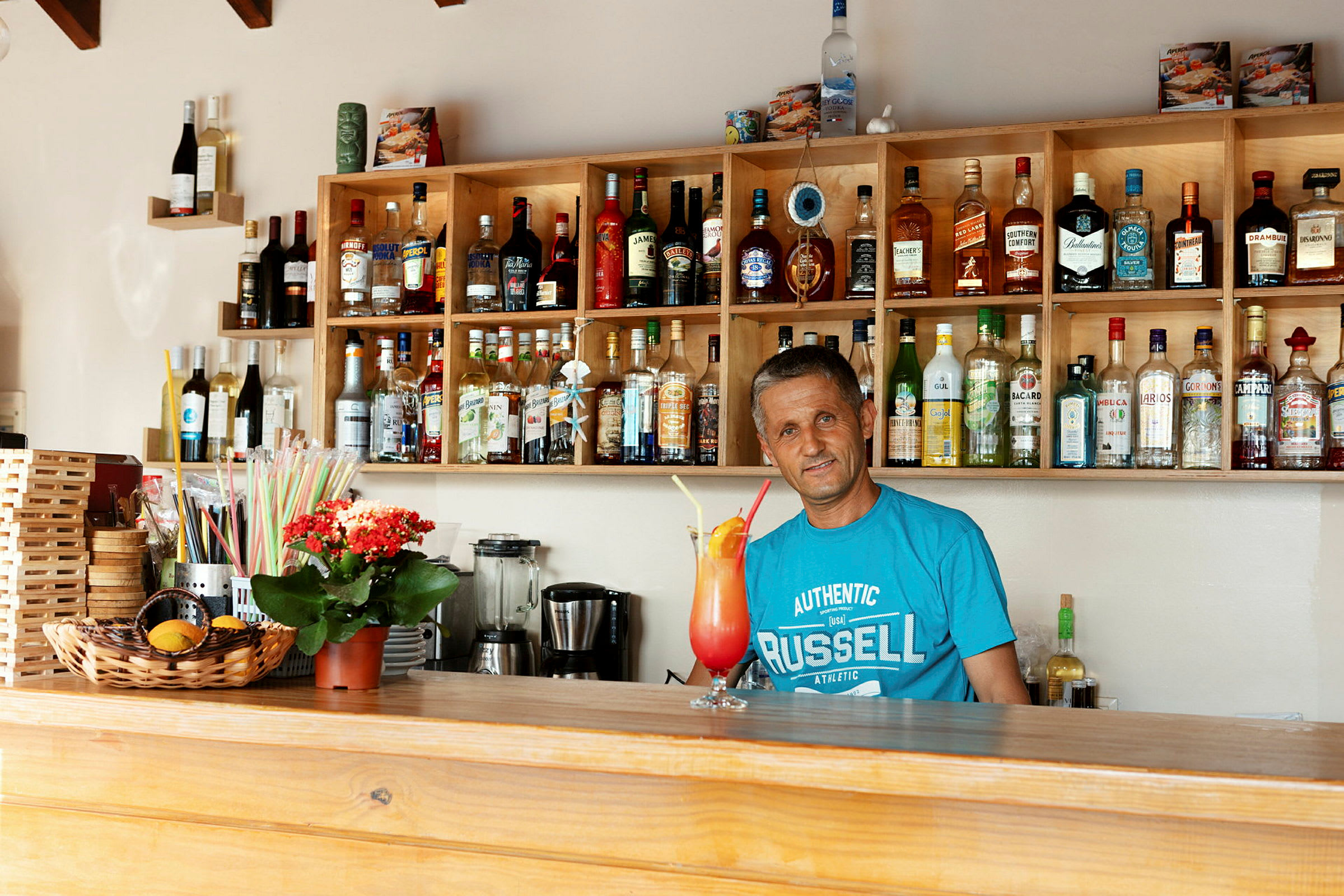 En bar med hyllor fyllda av alkoholflaskor och ett serveringsområde med en färgglad drink. (AI-genererad text)