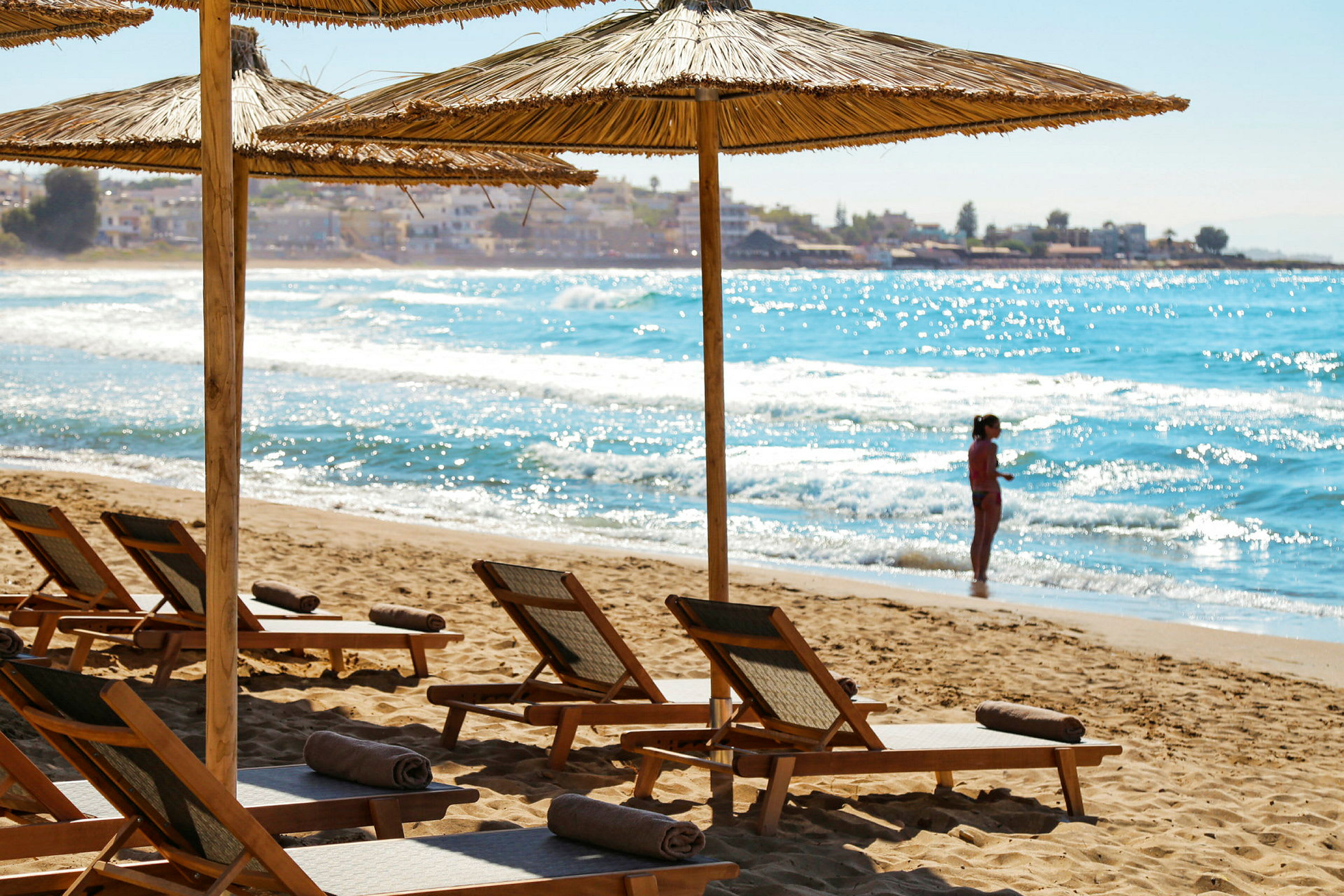 Strand med solstolar och parasoller, person som står vid vattenbrynet. (AI-genererad text)