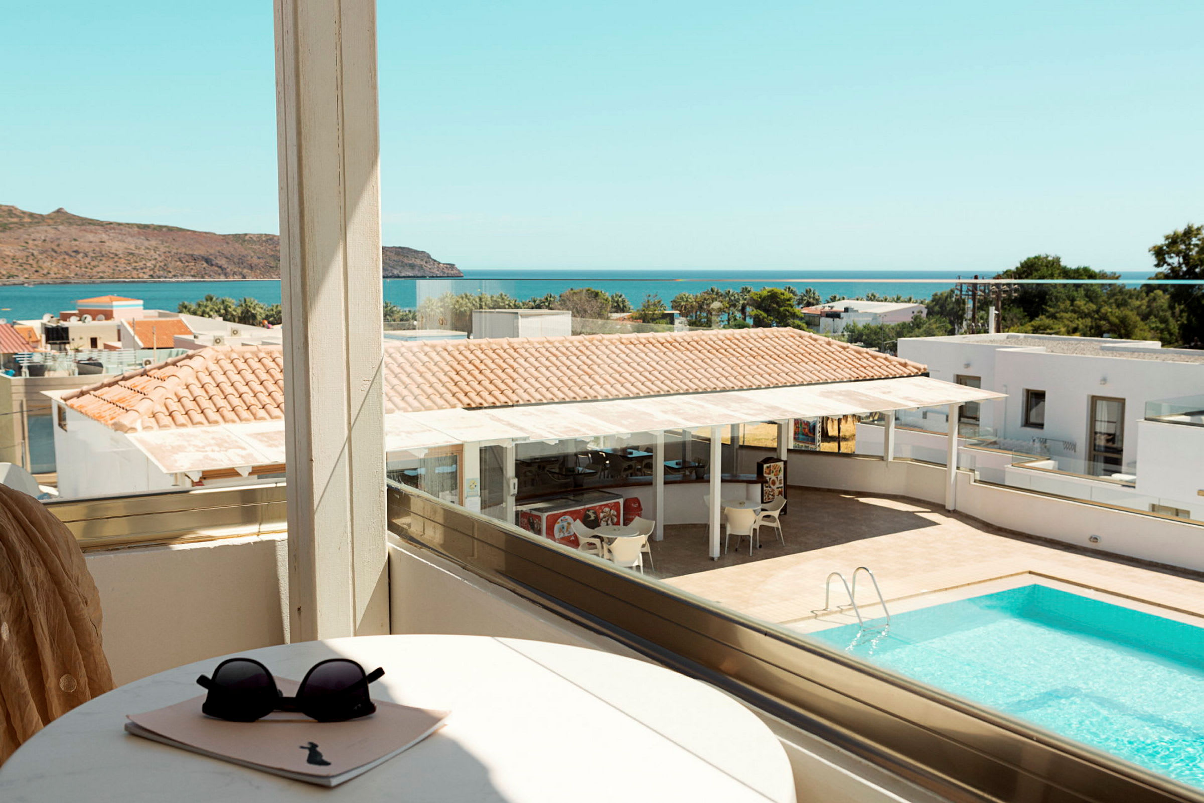Utsikt från en balkong över en pool, delar av ett hotellområde och havet i bakgrunden. (AI-genererad text)