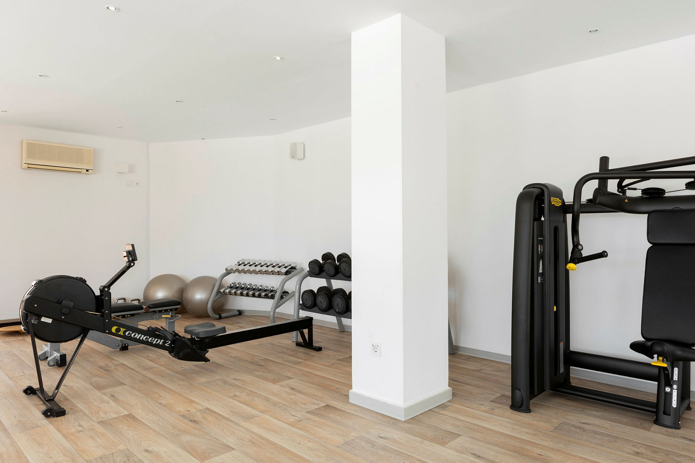 Ett gymrum med träningsmaskiner, hantlar och gymbollar på ett trägolv. (AI-genererad text)