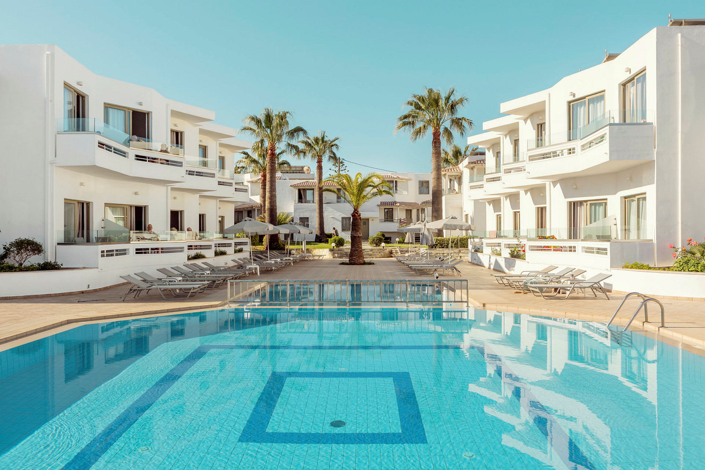 En utomhuspool vid ett hotell med vita byggnader och palmer. (AI-genererad text)