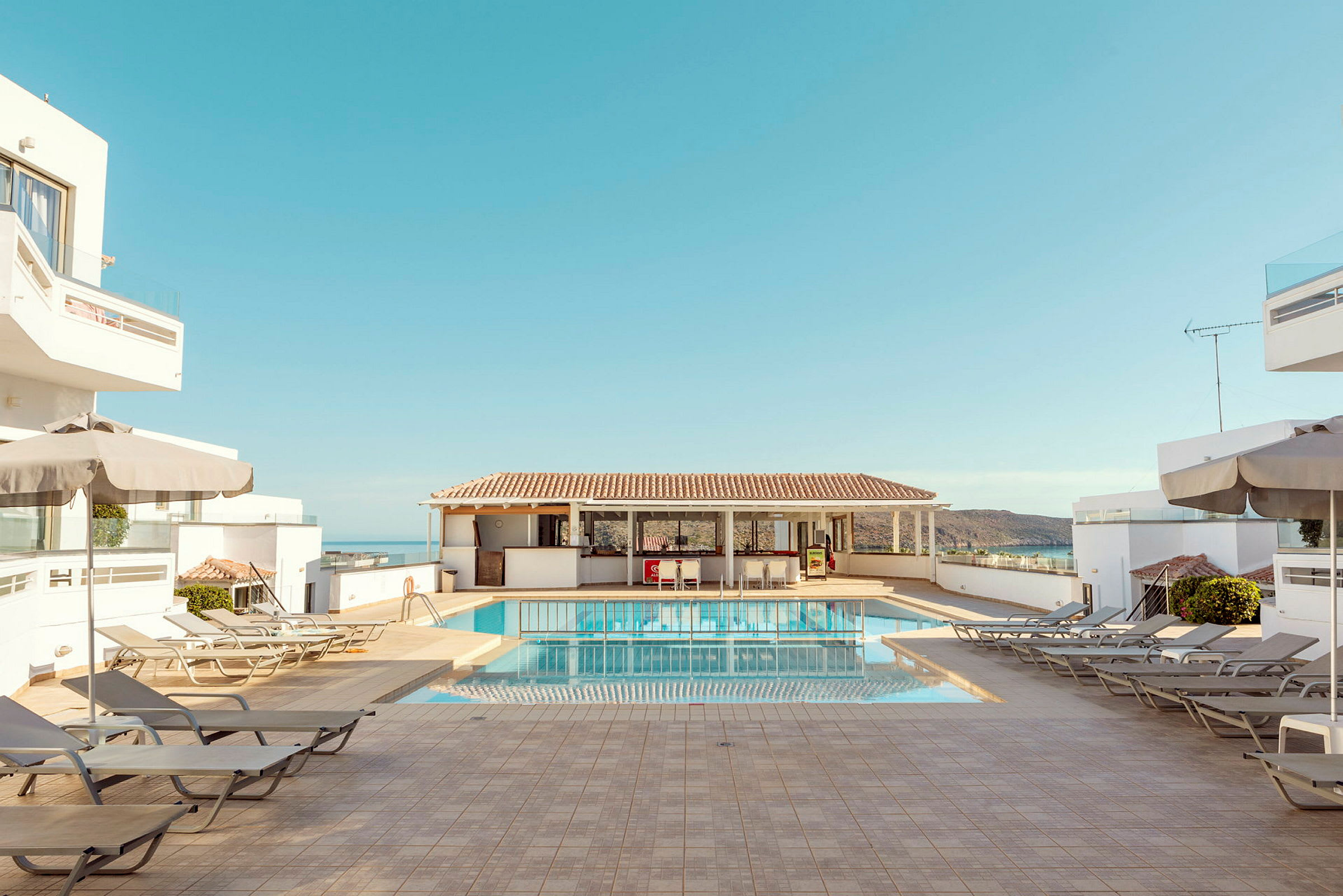 Hotellpoolområde med solstolar, parasoller och blå himmel. (AI-genererad text)