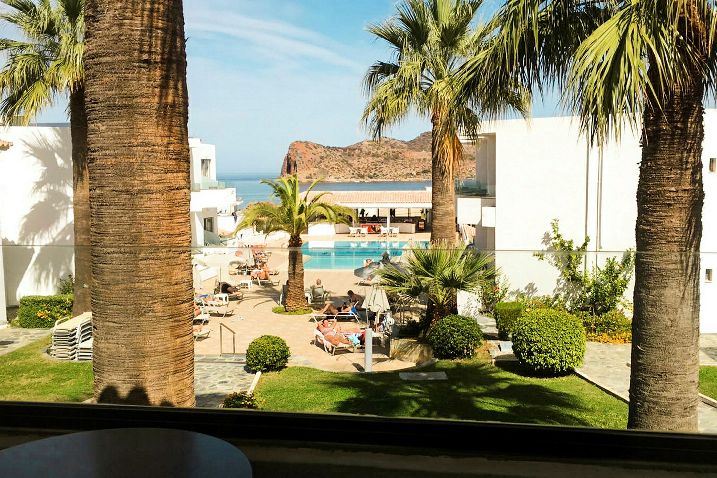 Hotellområde med pool och palmer, utsikt över havet och klippor i bakgrunden. (AI-genererad text)
