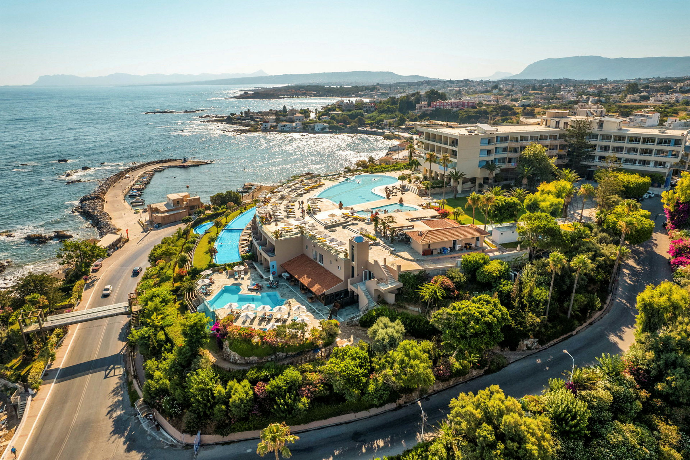 Flygfoto av en resort vid havet med pooler, byggnader och grönska. (AI-genererad text)