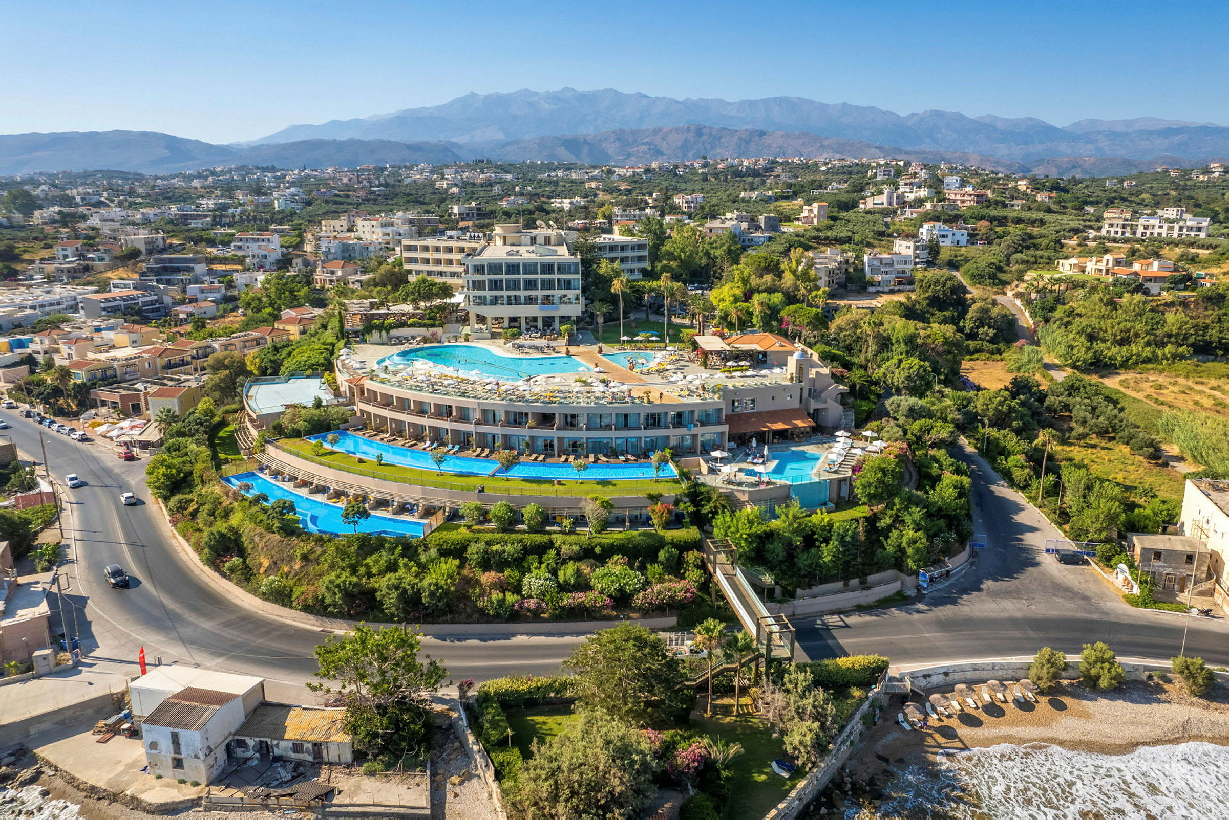 Flygbild av ett hotellområde med pooler, omgiven av andra byggnader och grönska. (AI-genererad text)