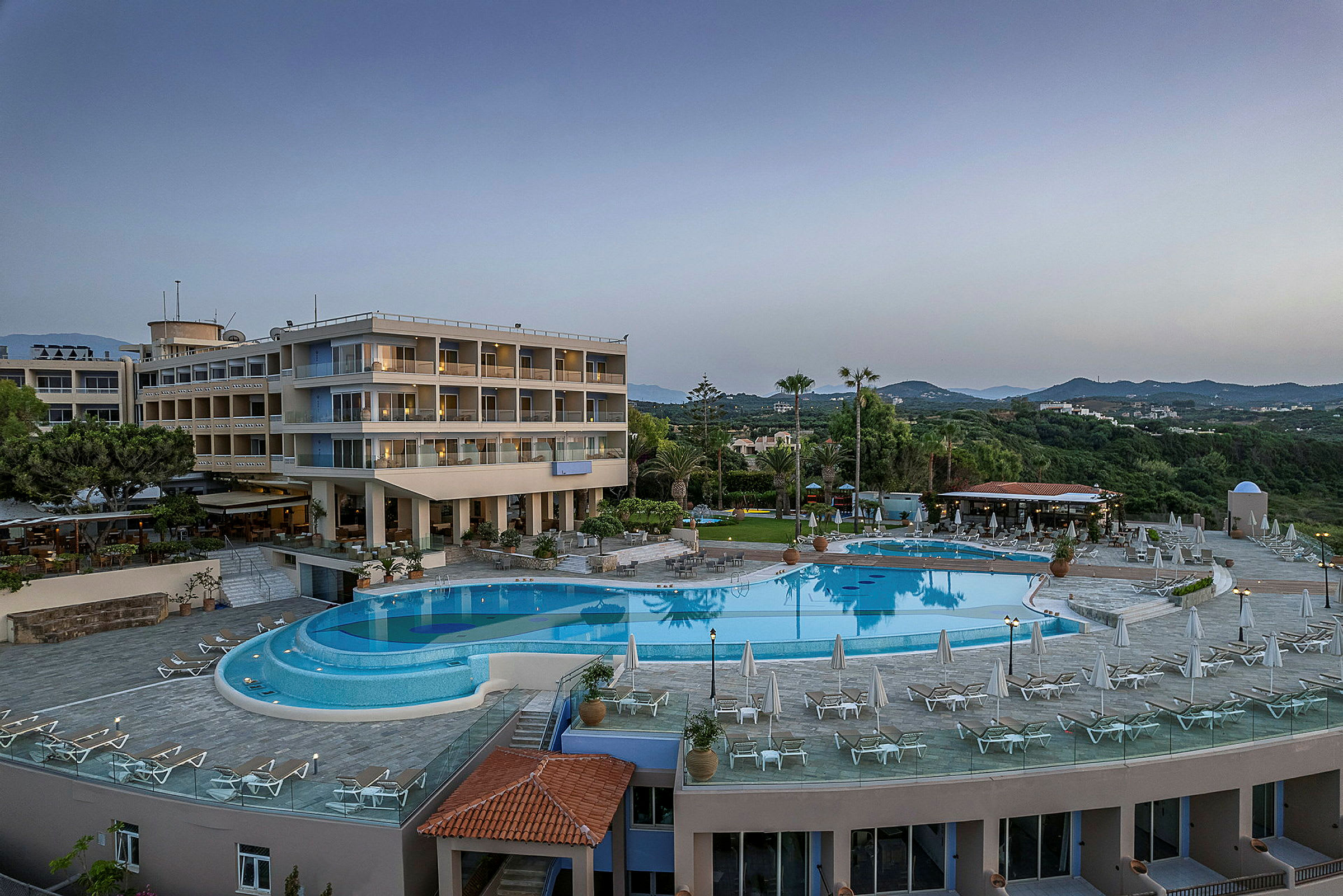 Hotell med flera våningar, swimmingpool och solstolar i en grönskande miljö. (AI-genererad text)