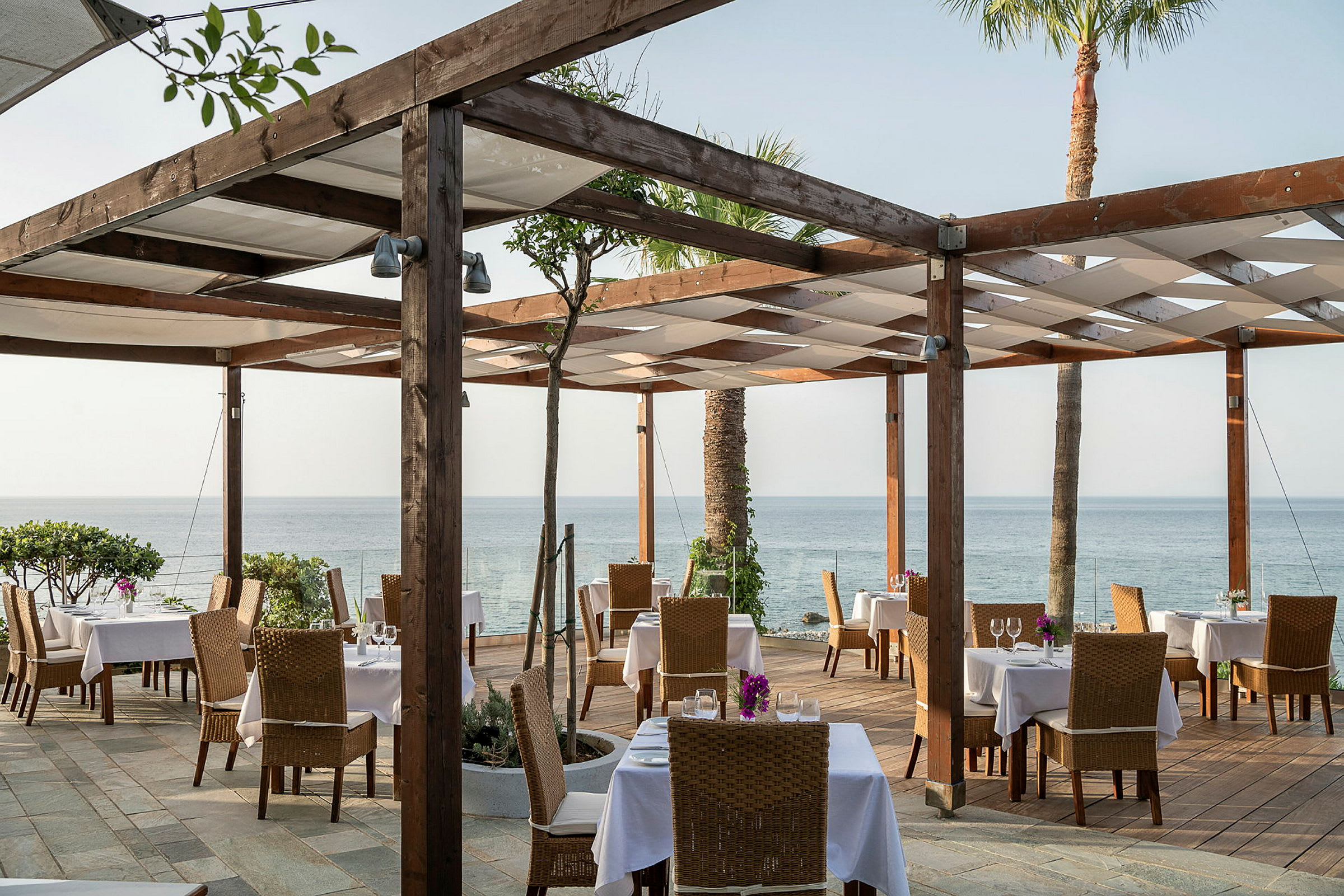 Restaurang med utomhusservering, bord och stolar, och utsikt över havet. (AI-genererad text)