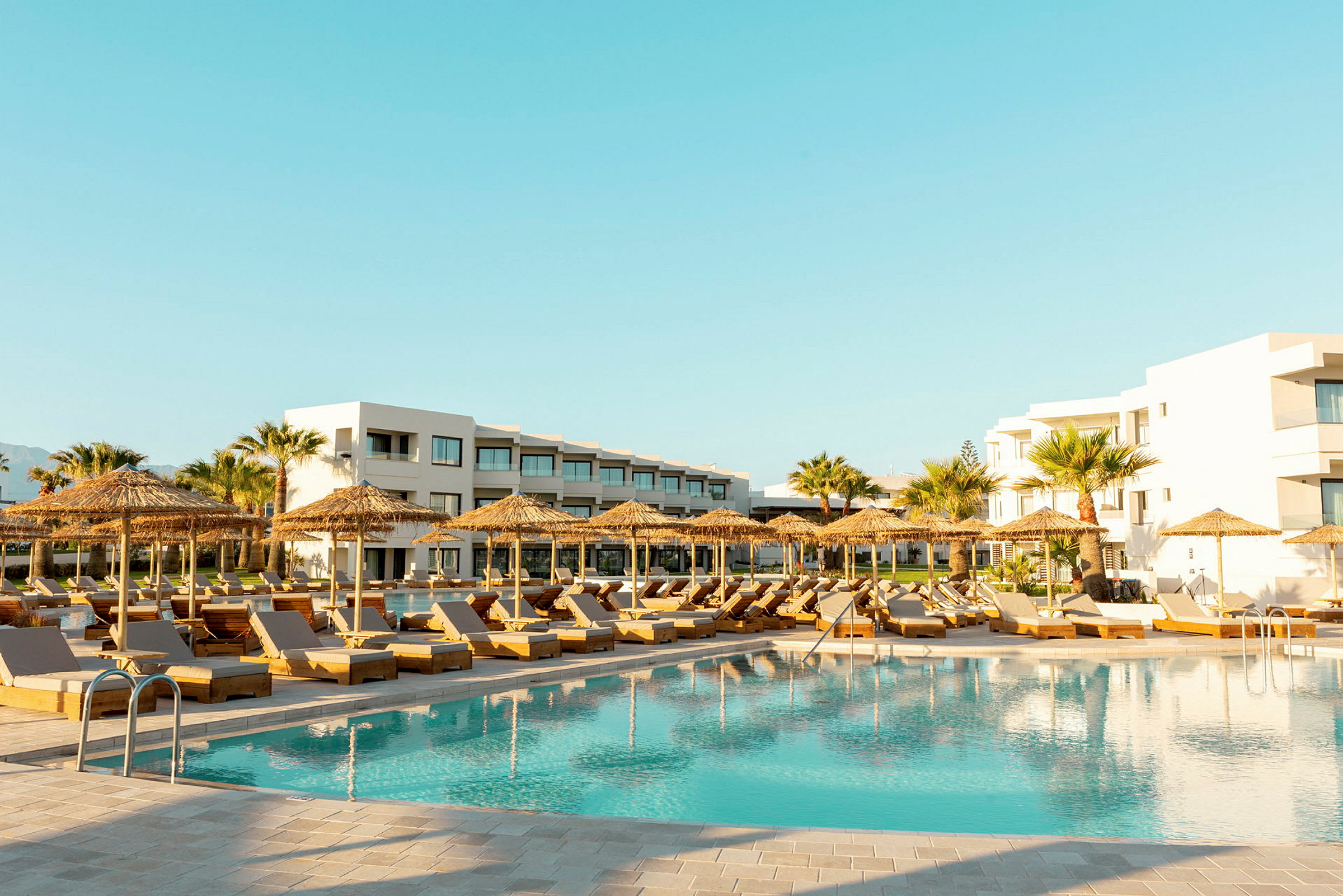 Poolområde med solstolar, parasoller och moderna hotellbyggnader i bakgrunden. (AI-genererad text)