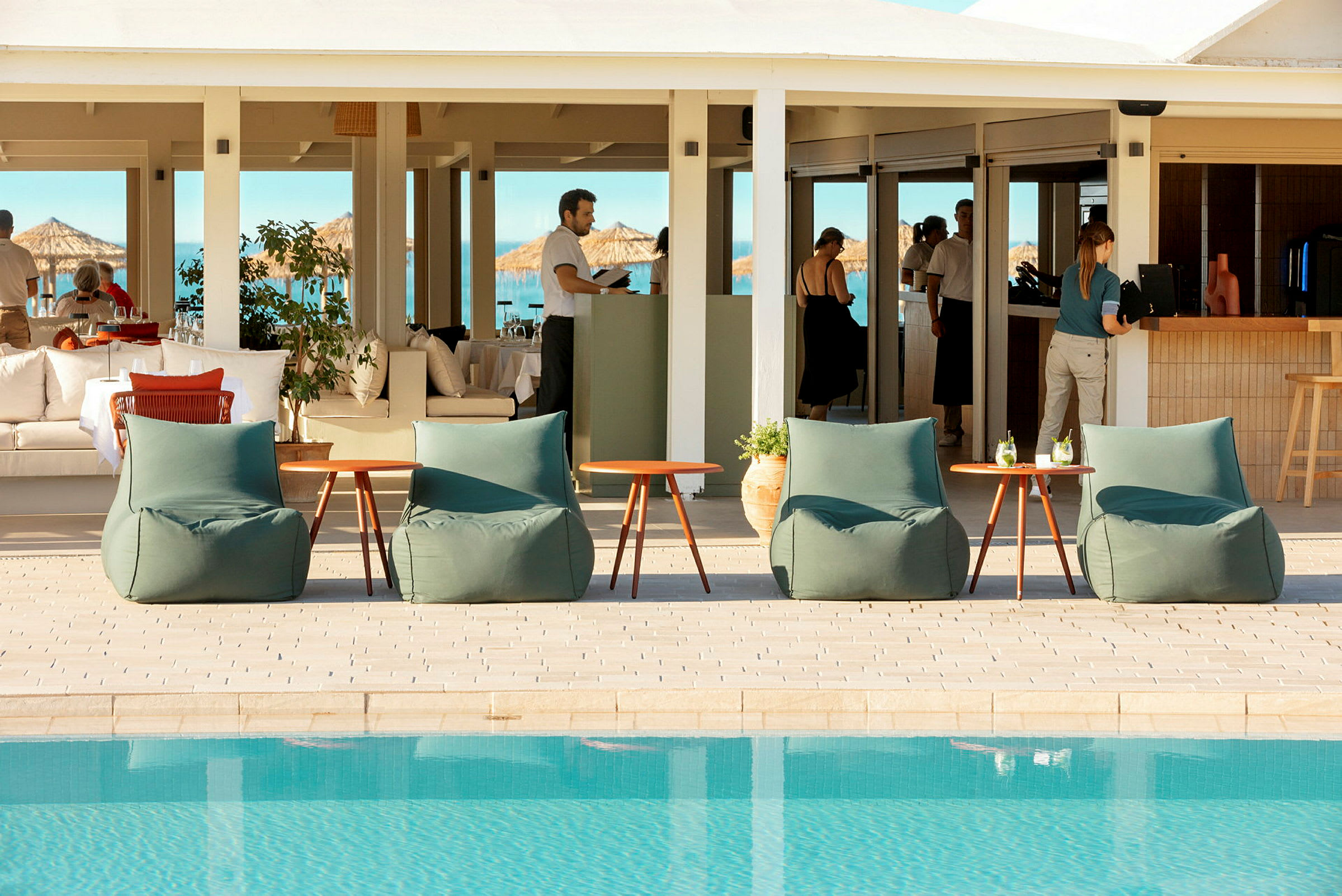 Utemöbler vid en pool med en restaurang i bakgrunden. (AI-genererad text)