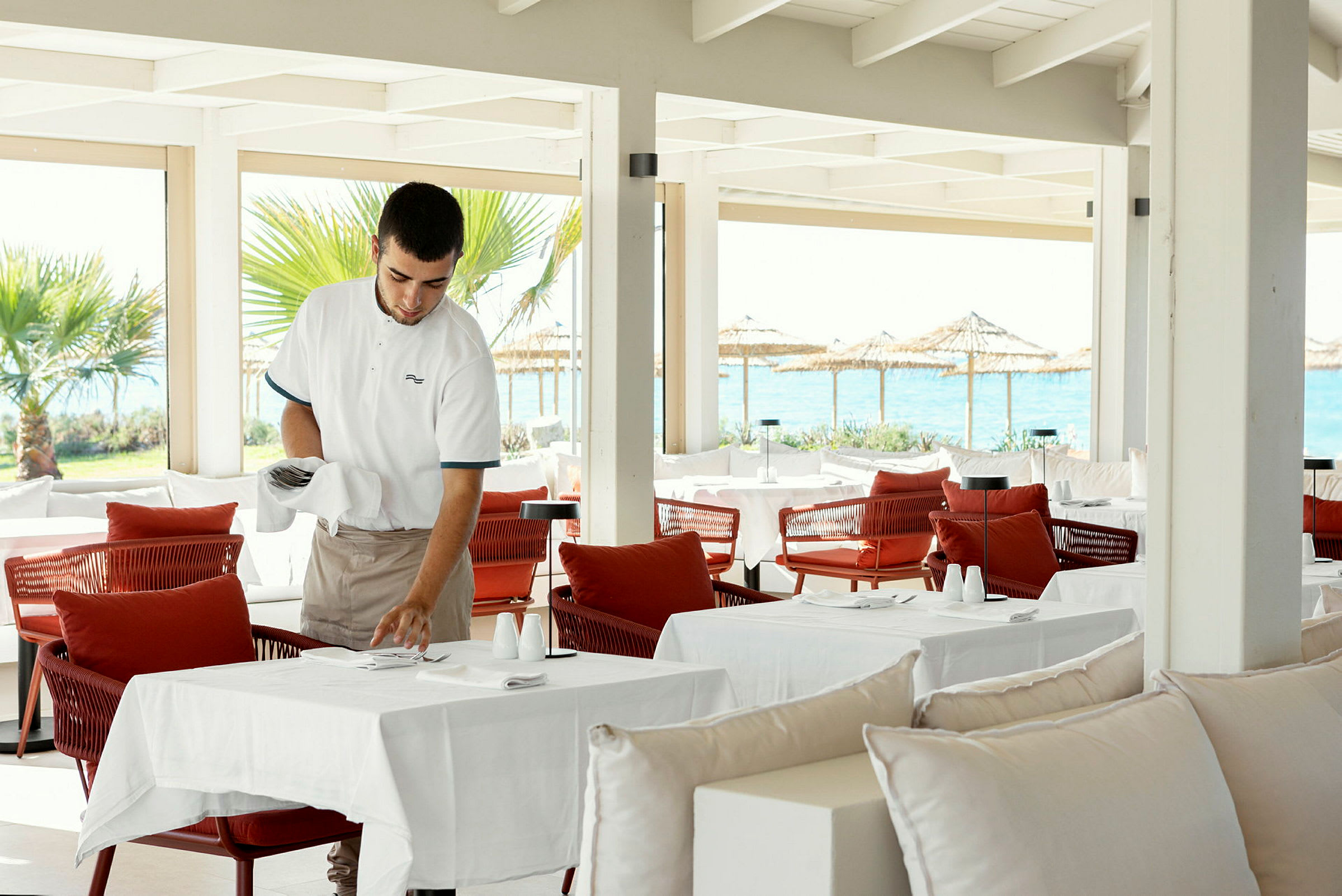 Serveringspersonal förbereder dukning på en restaurang med havsutsikt. (AI-genererad text)
