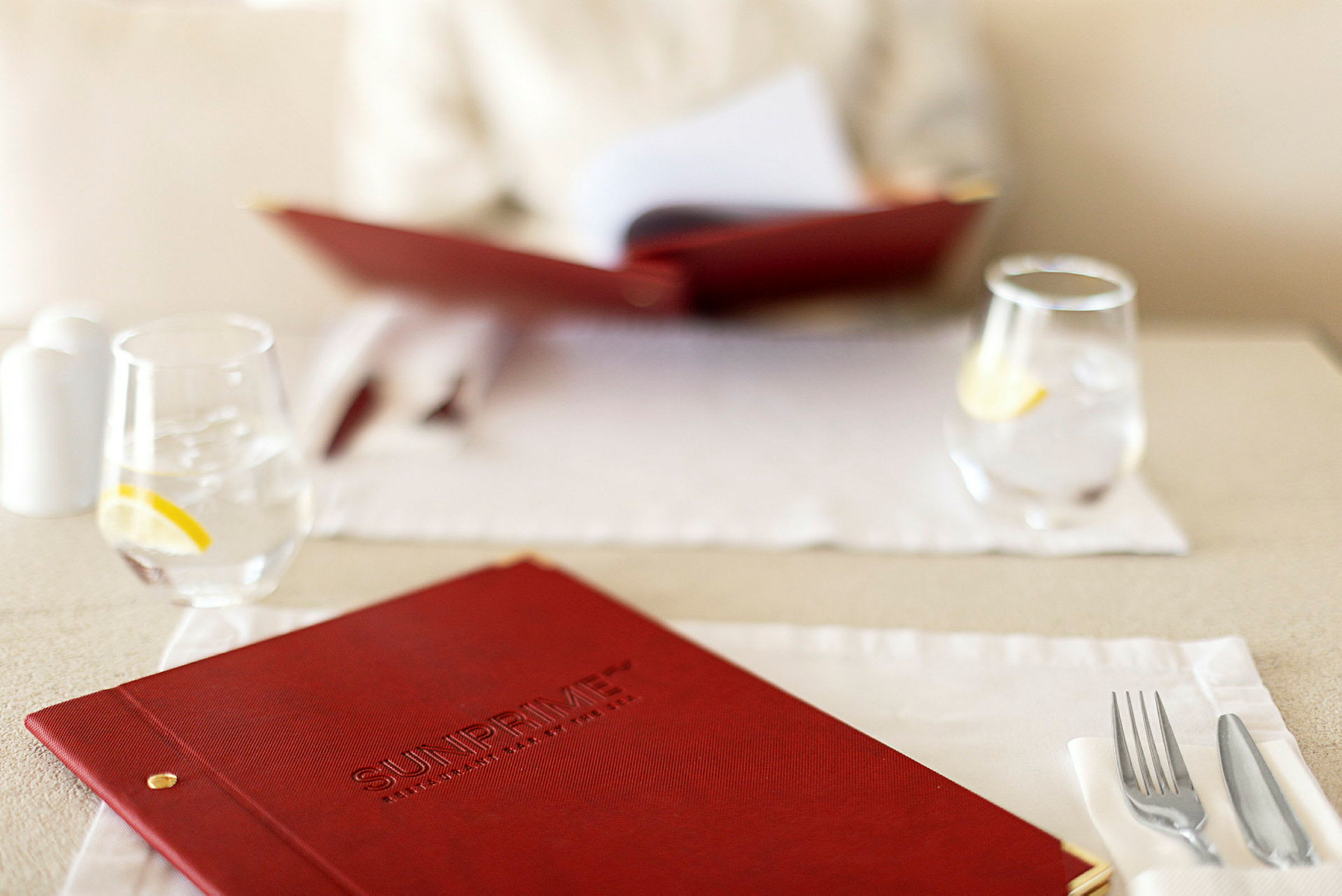 Närbild av en röd menybok på en dukad restaurangbord med glas och bestick. (AI-genererad text)