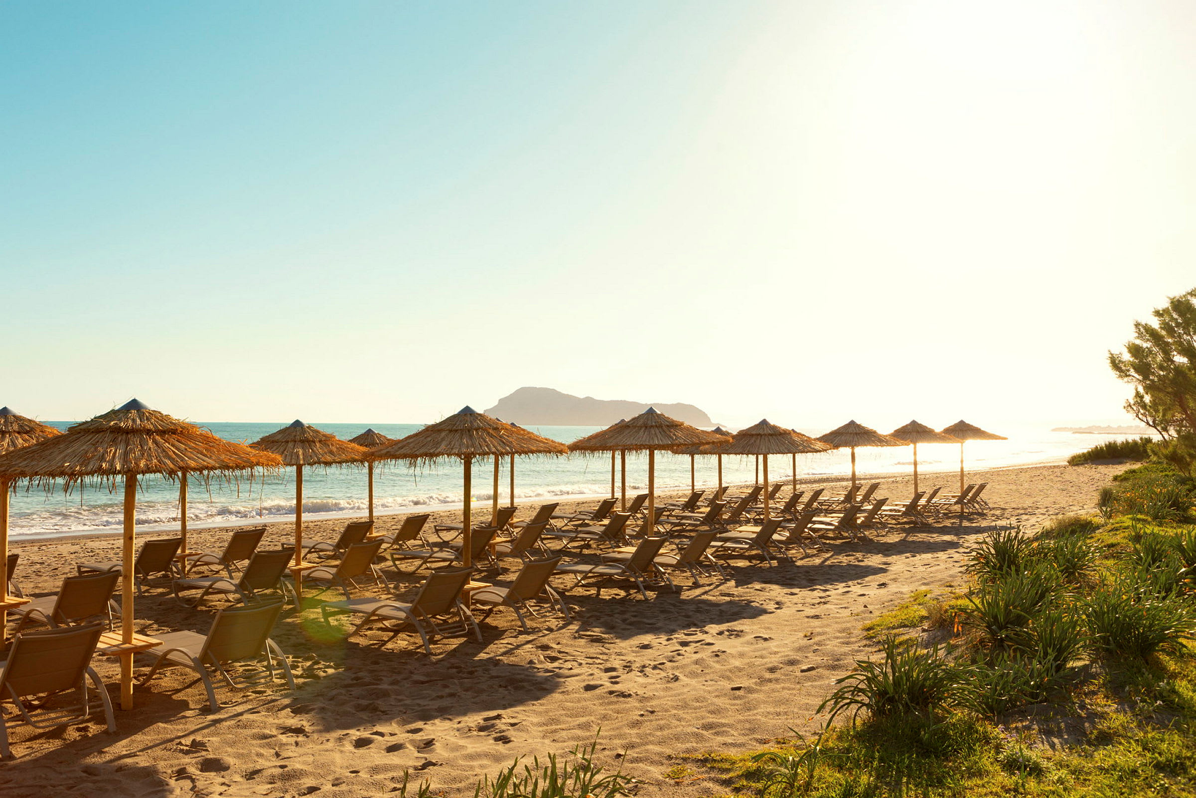 Strand med solstolar och parasoller av halm vid vattnet. (AI-genererad text)