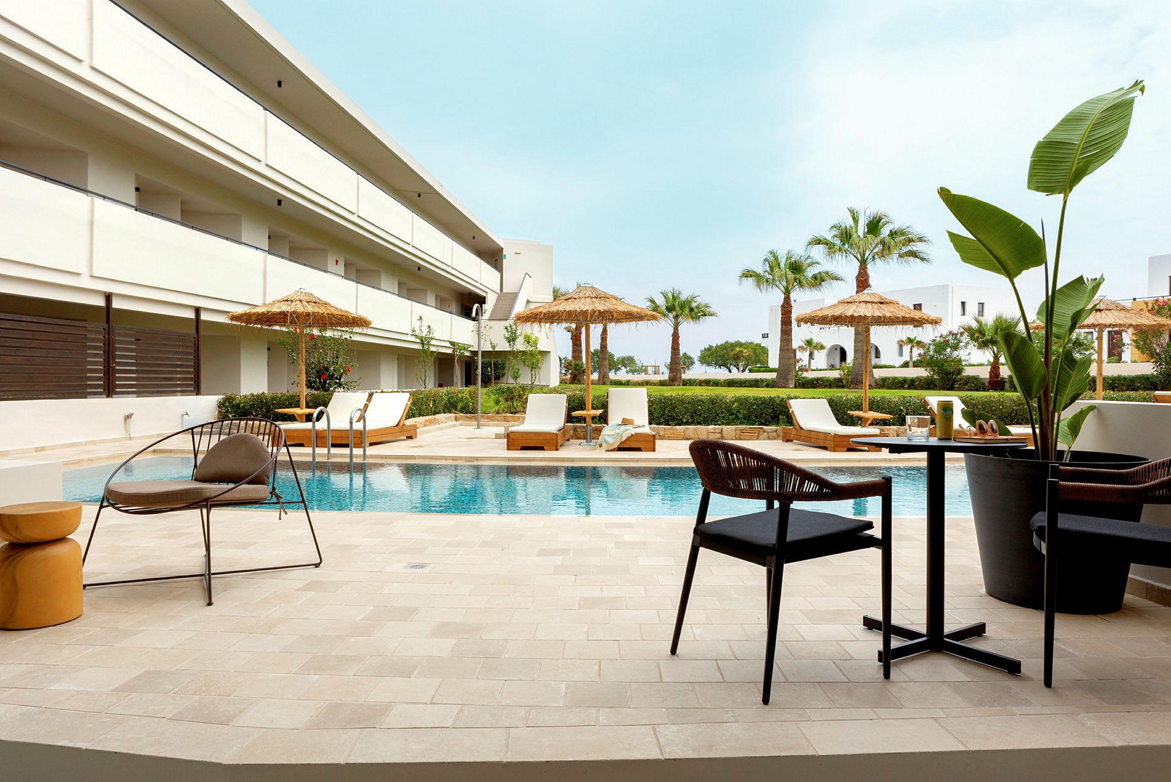 Hotellpool med solstolar och parasoller omgivna av palmer. (AI-genererad text)