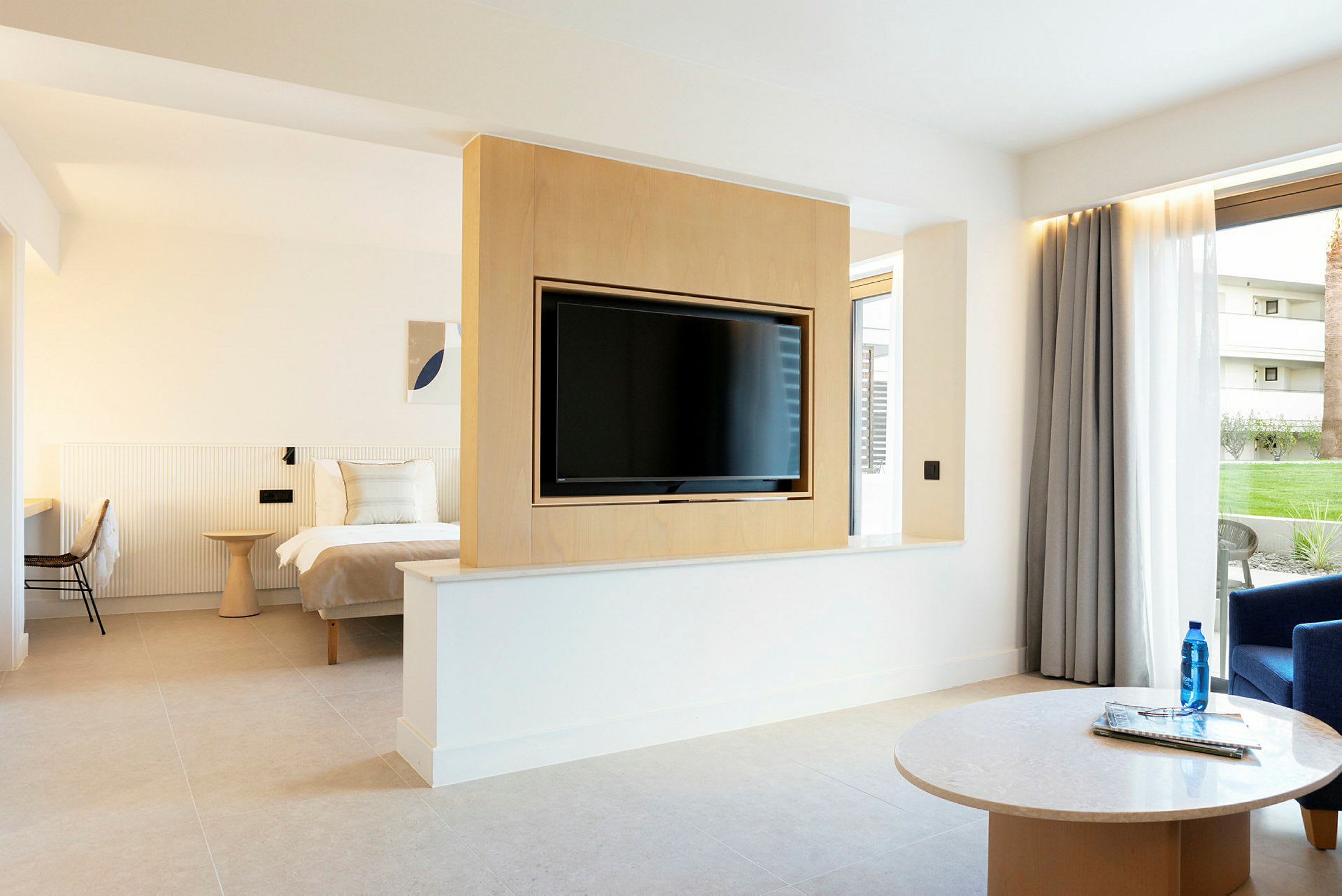 Ett hotellrum med en dubbelsäng, en tv monterad på en träpanel och en sittgrupp med ett bord. (AI-genererad text)