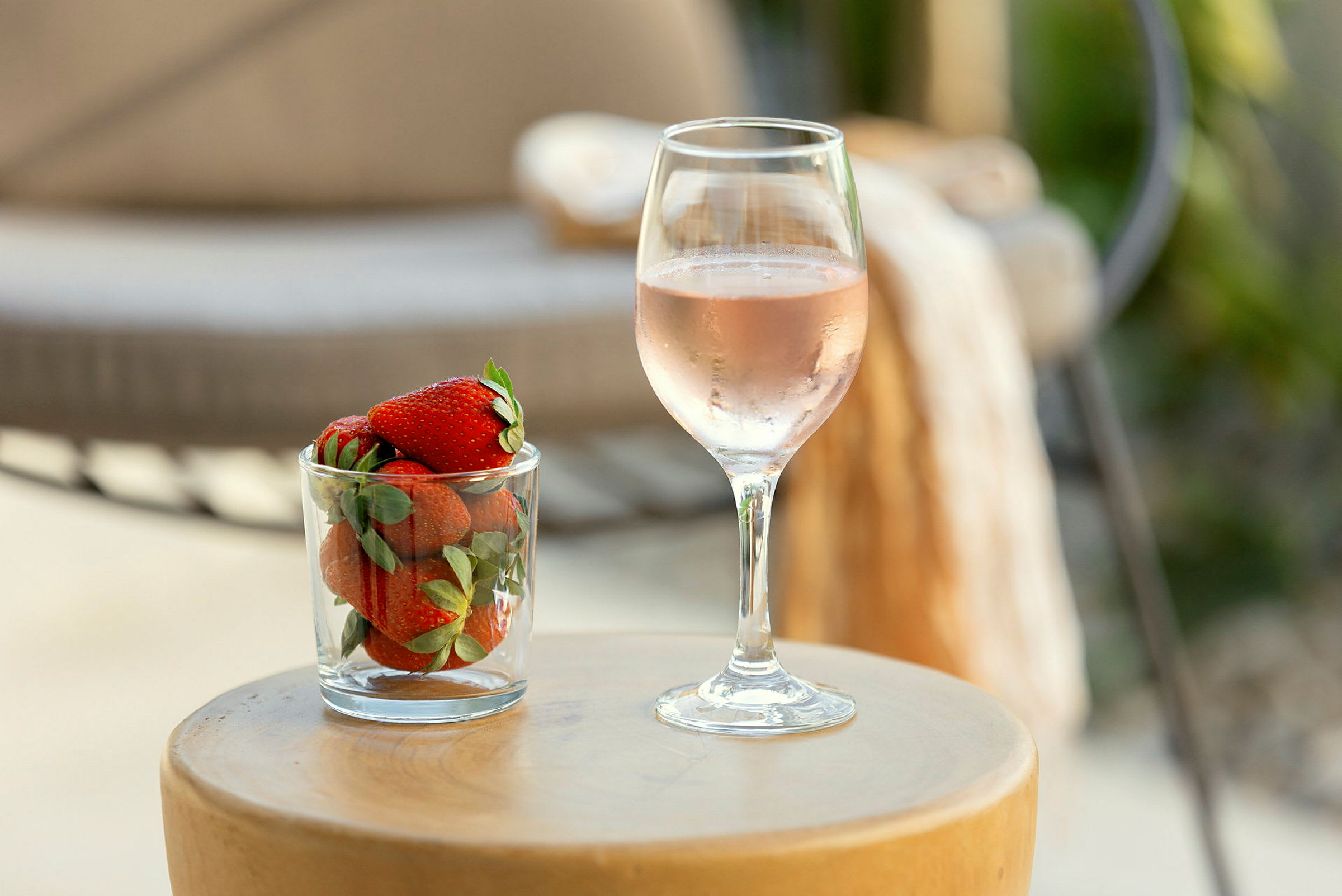 Ett glas med jordgubbar bredvid ett glas rosévin står på ett runt bord. (AI-genererad text)